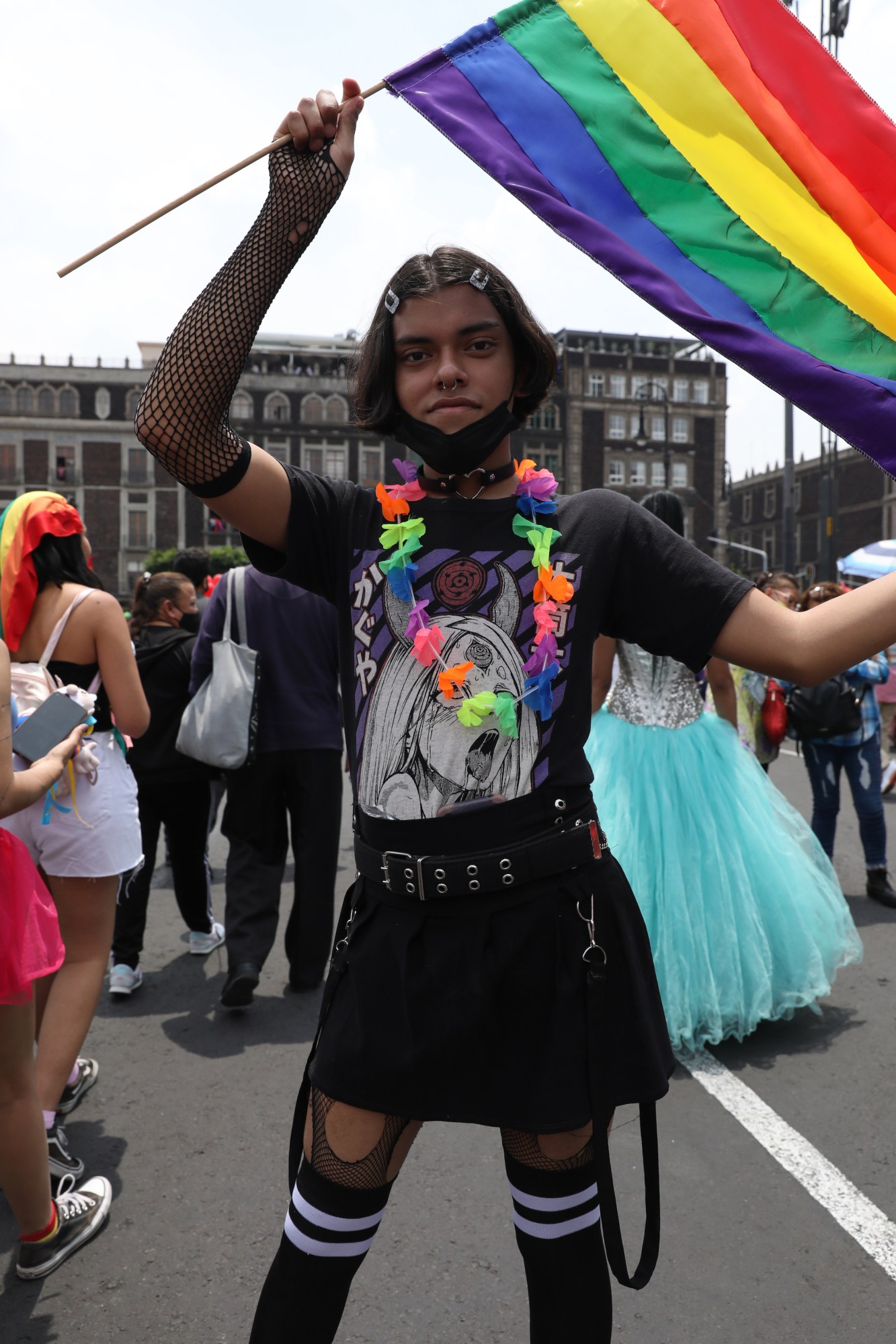 person in all black and a rainbow garland waving a pride flag at Mexico Pride 2022