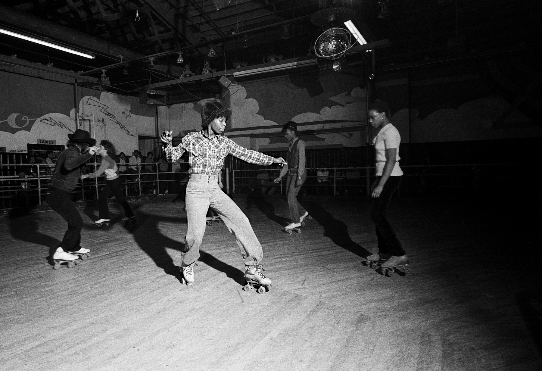 black-and-white photo of roller disco dancers on wooden floor in circle