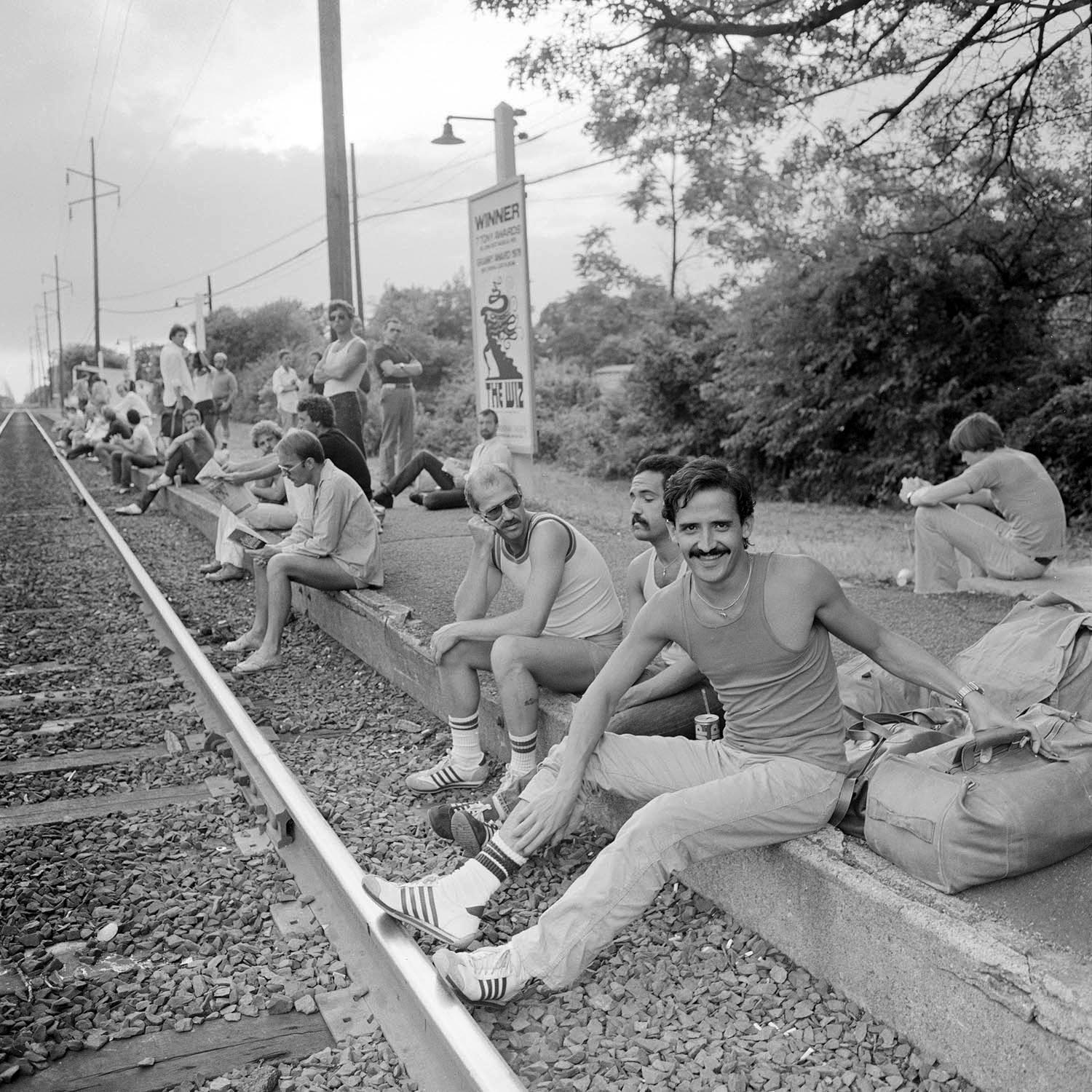 gay men sit on the train tracks in the 1970s wearing vests and sneakers