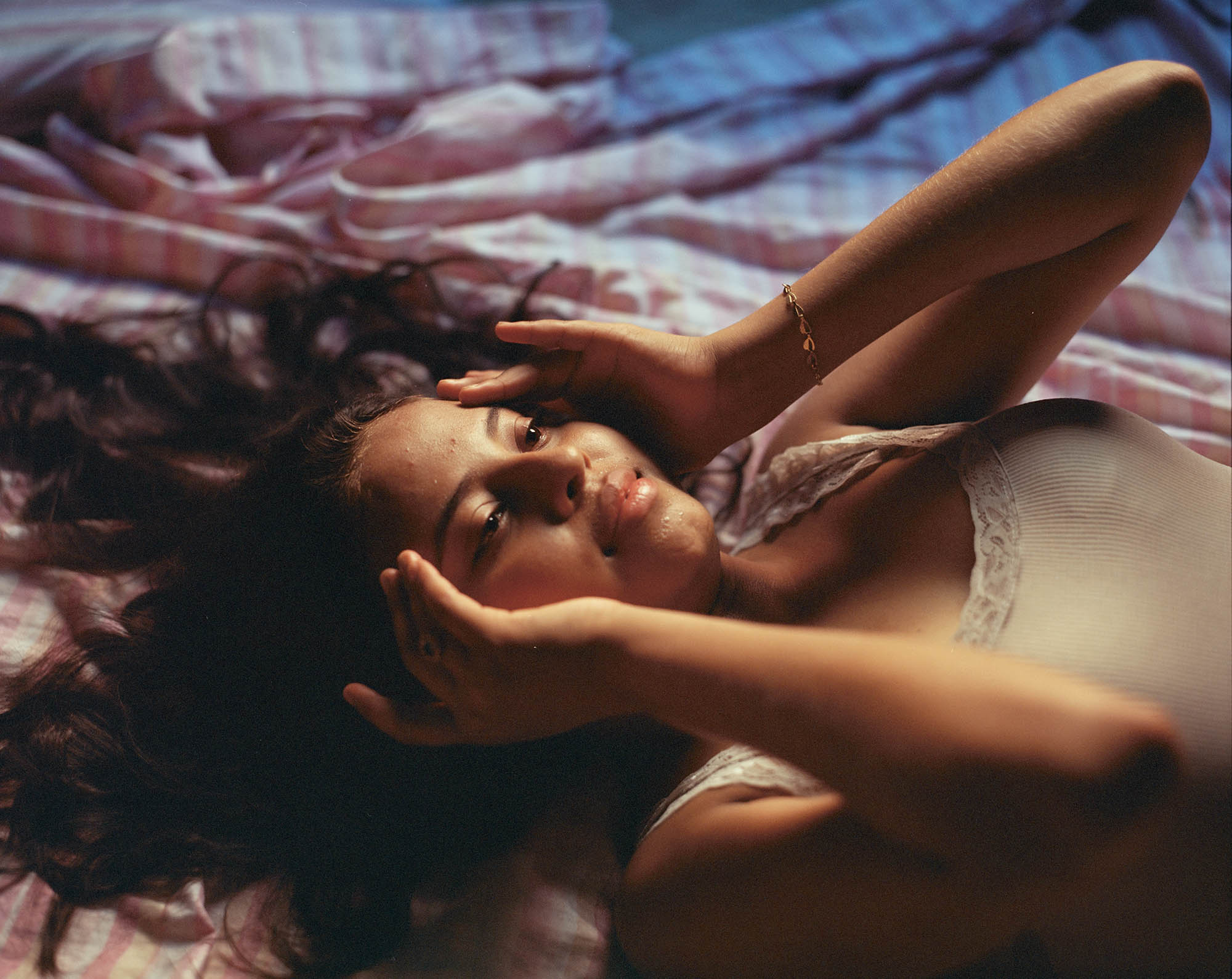 A young person lying on a bed while pressing their fingers on their temples.