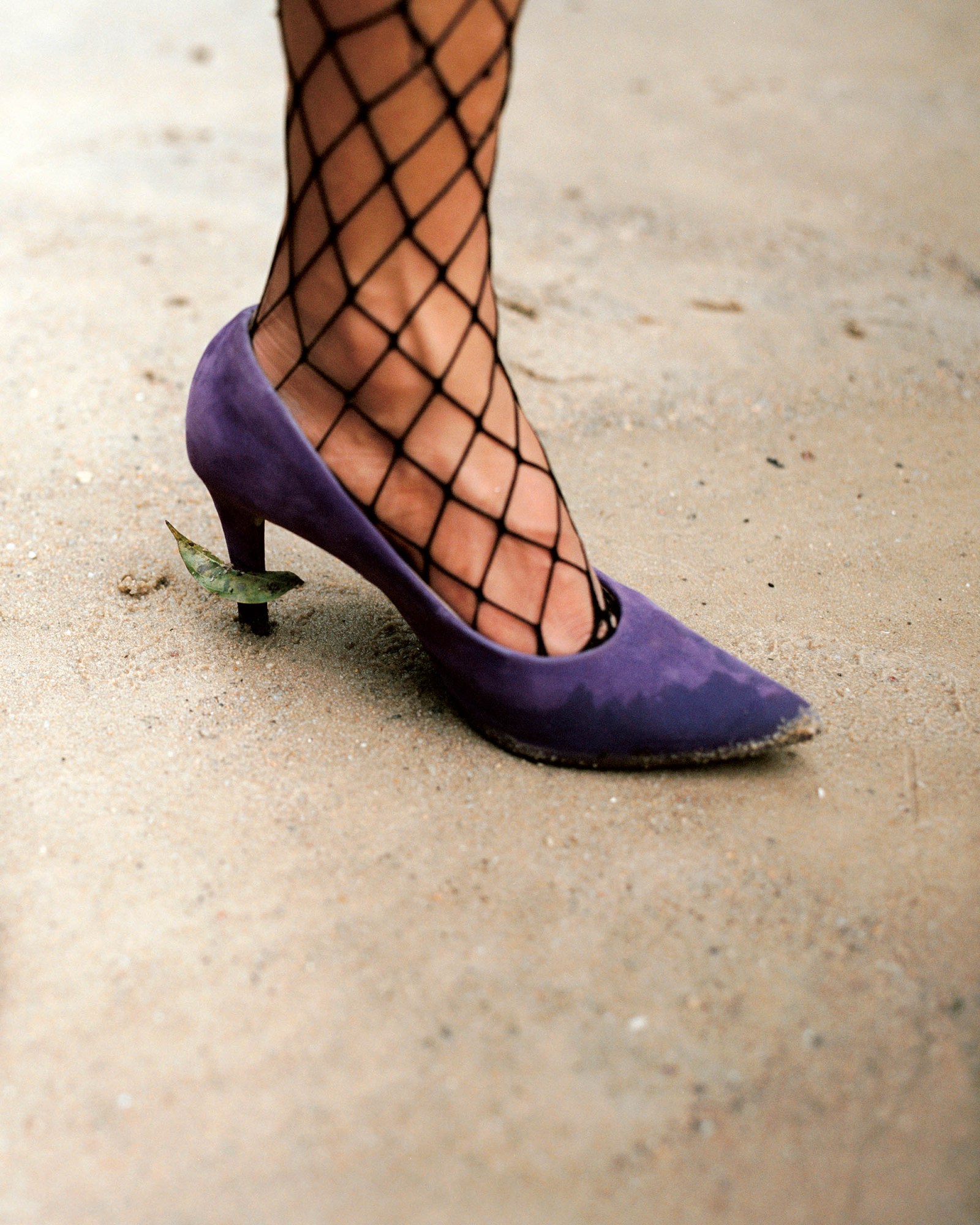 A foot wearing a purple high heeled pump and black fishnet tights.