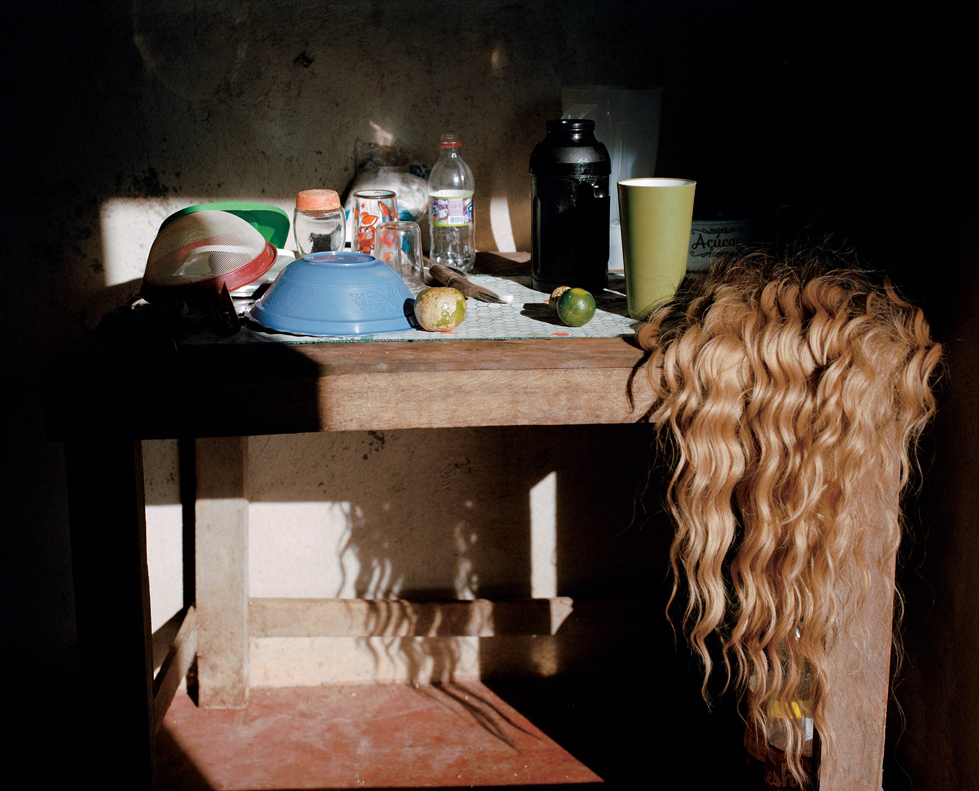 A wooden table covered in bowls, bottles, and a blong wig.