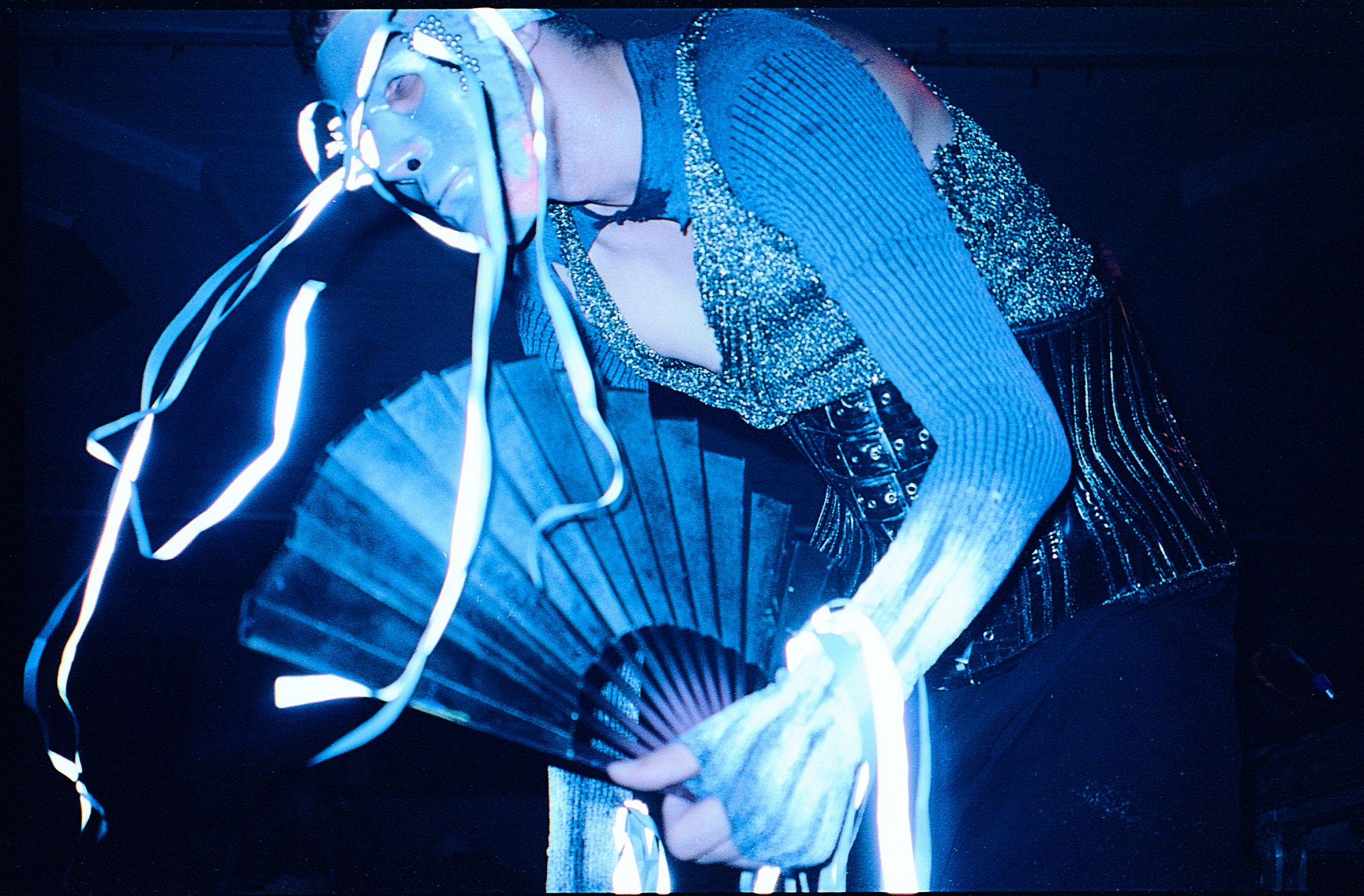 someone wearing a mask with streamers and holding a fan at a rave in brazil