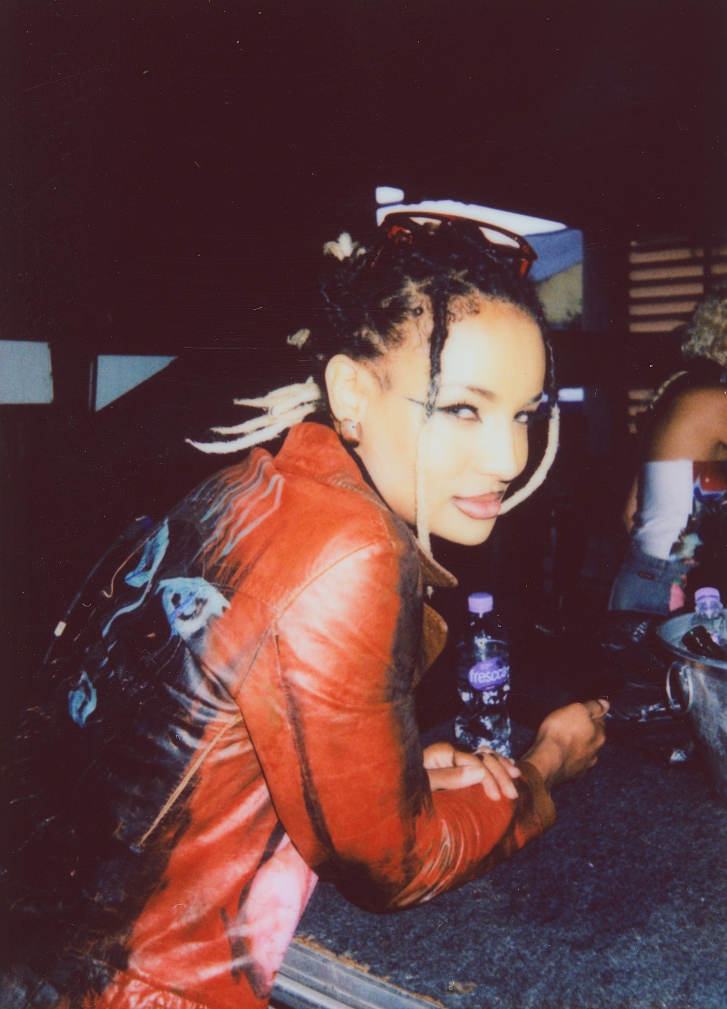 a girl in a red jacket with braids leaning on a bar