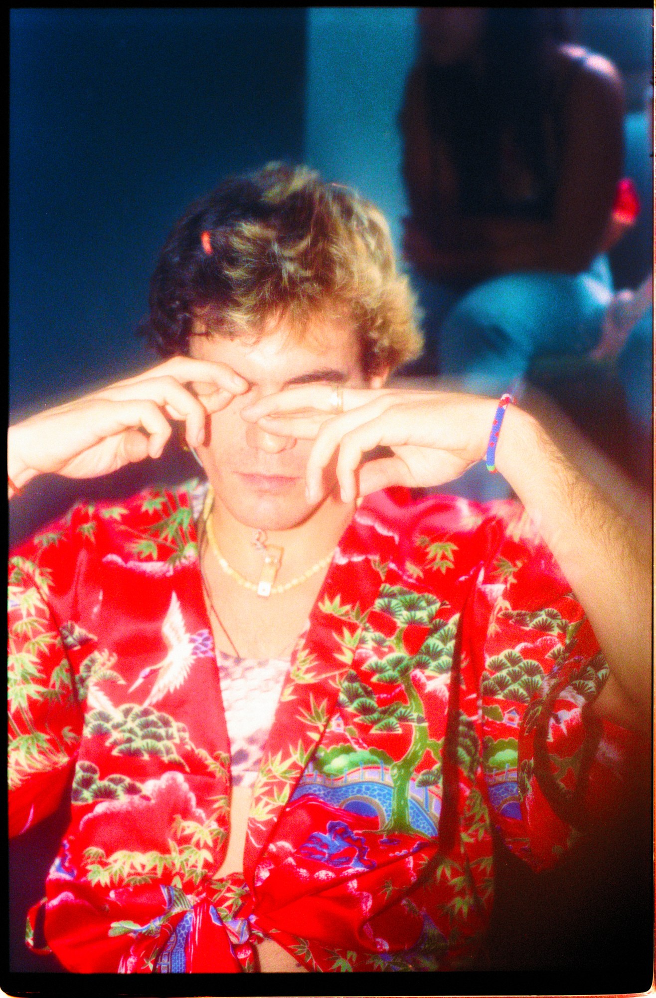 a guy with a red floral shirt holding his fingers up to his eyes