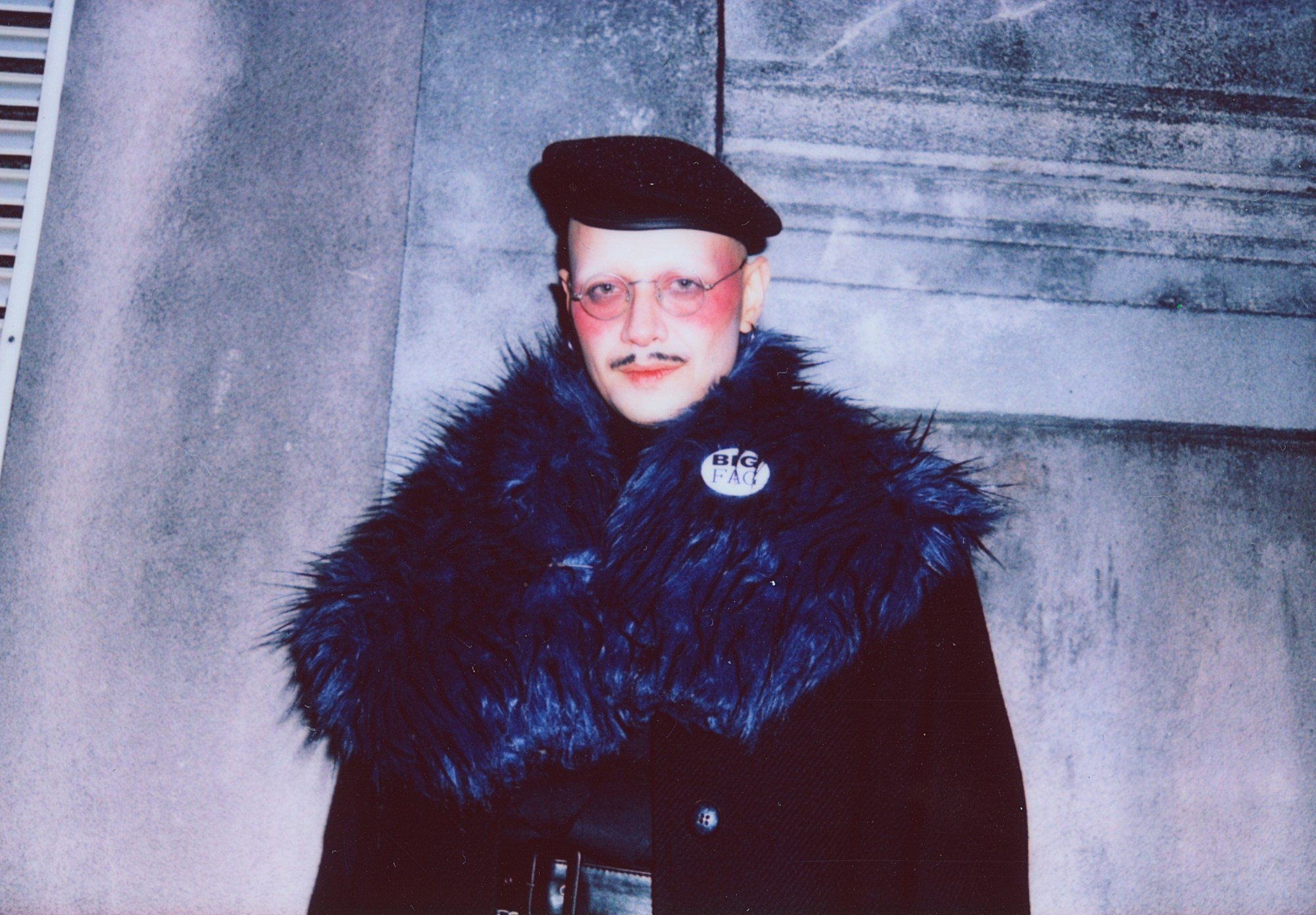 a man wearing a fur coat and face makeup with a beret standing outside a rave in brazil