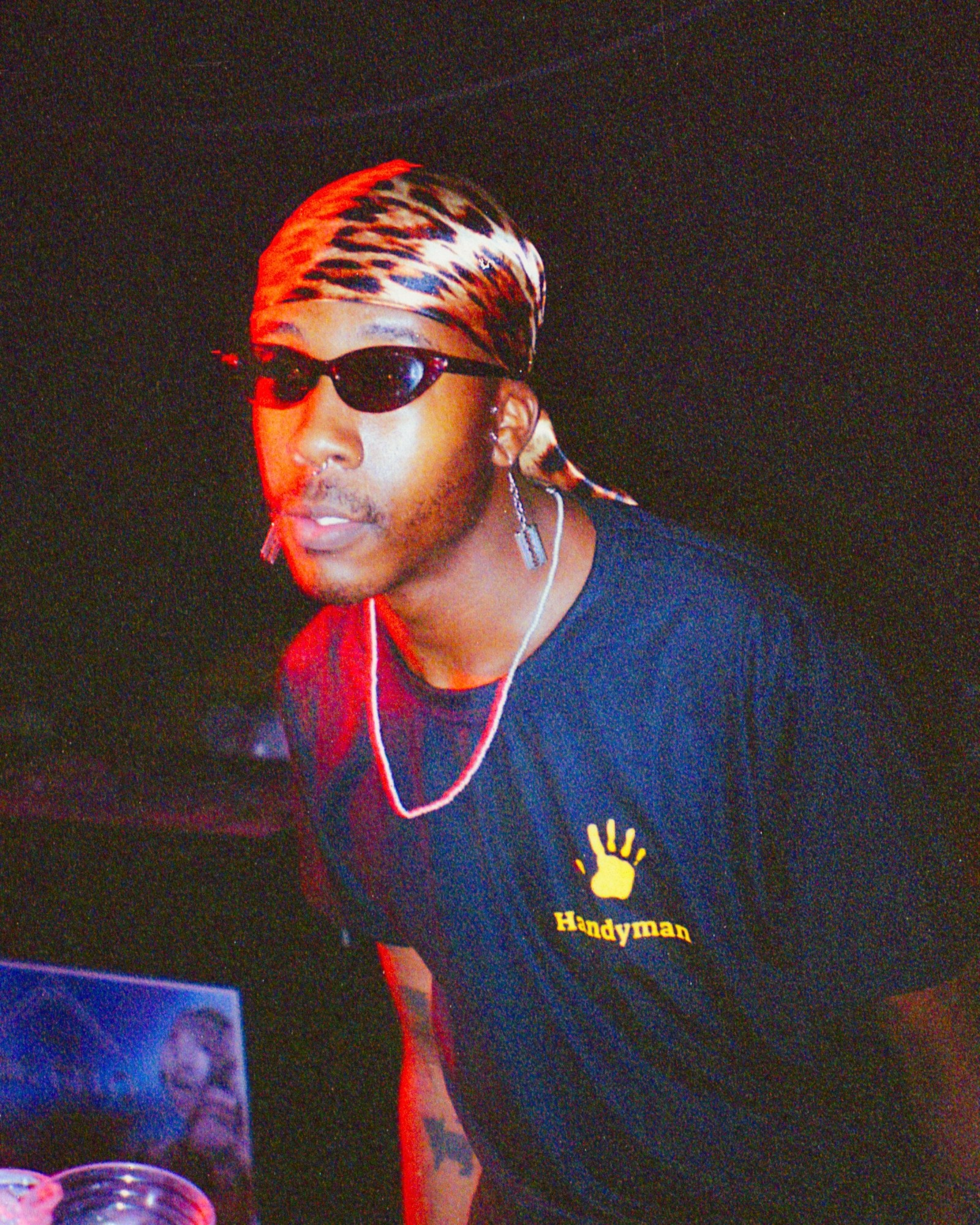 a man with a leopard silk bandana and chain wearing a handyman tshirt