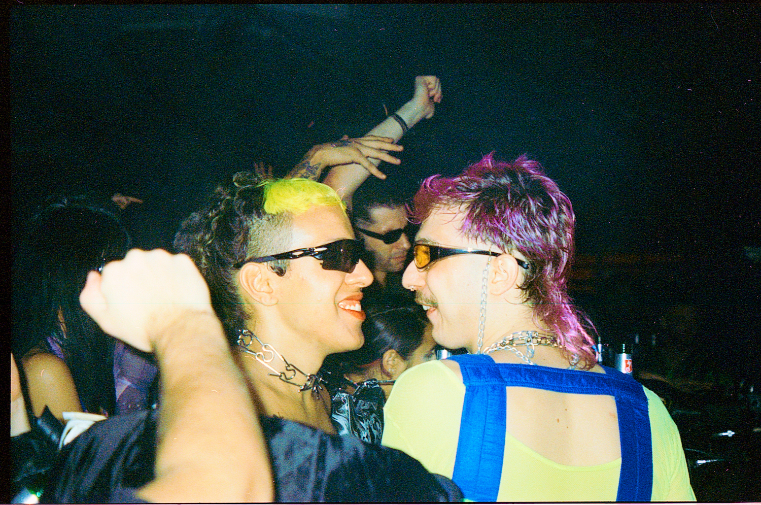 c couple with rainbow hair and sunglasses looking into each other's eyes on the dancefloor