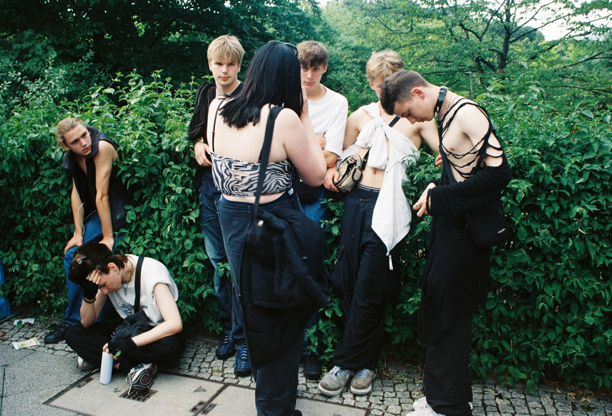 a group of young goths gather by a bush