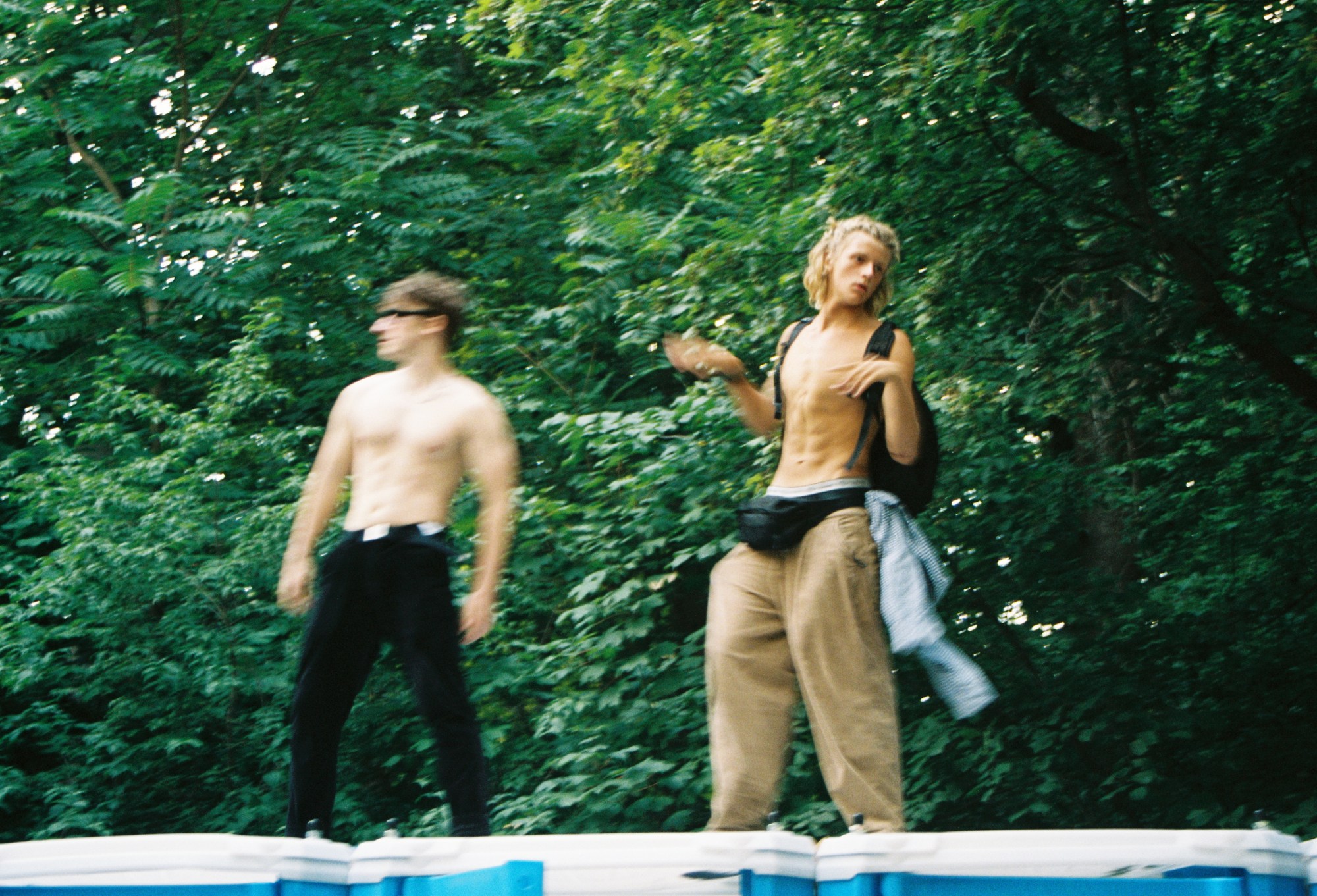 two young guys stand on the roof of some portaloos