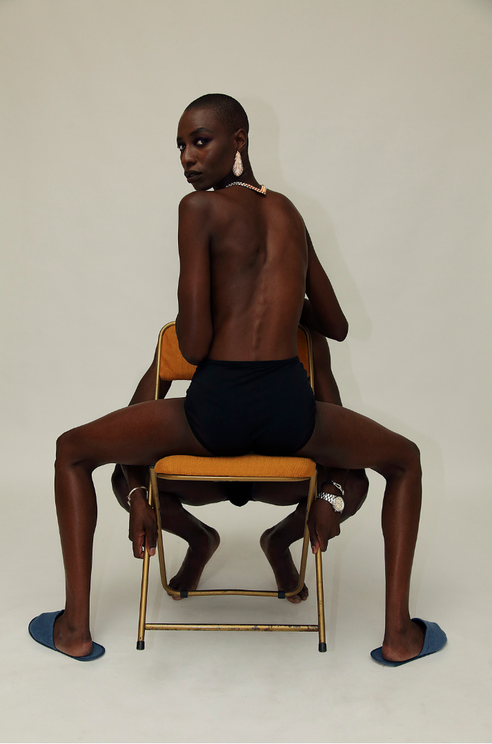 a topless woman shot from behind sitting on an orange chair