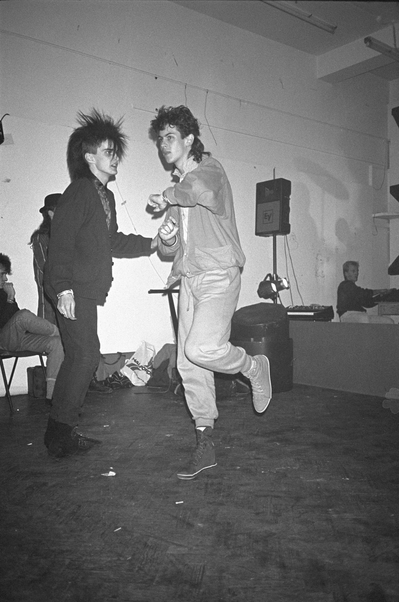 Black-and-white image of two punks dancing on an empty dance floor with a sound system behind them