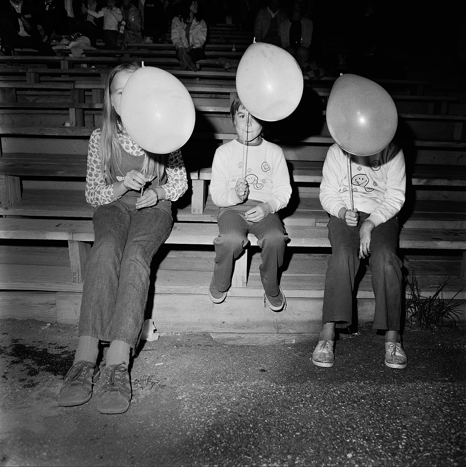 three children sit in a row, a balloon obscuring each of their faces