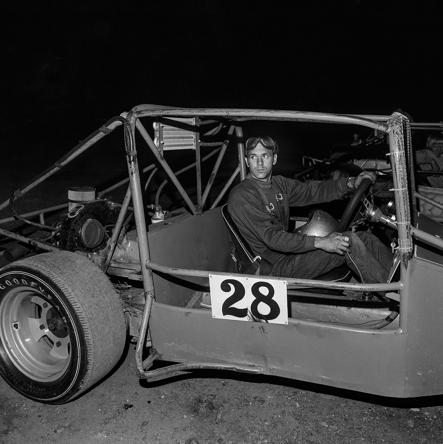 a race car driver looks off to the side of the frame as he turns his (number 28) vehicle