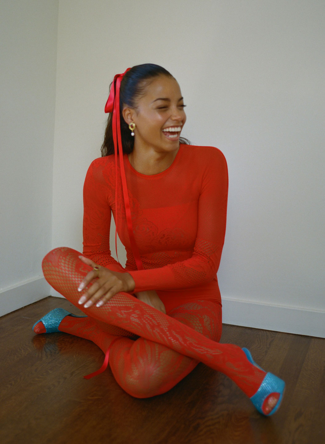 ella balinska laughing wearing a red fishnet bodysuit, paired with a long red ribbon in her hair