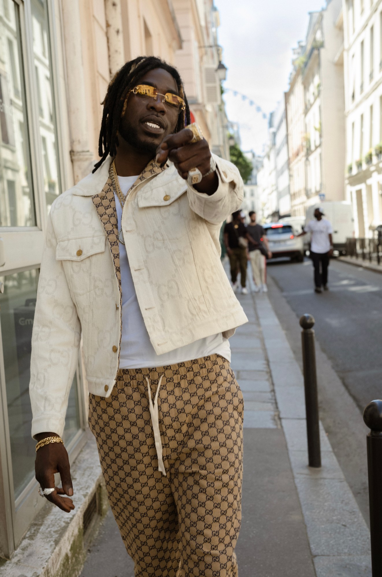 gazo, in a full gucci monogrammed look, walks down a street in paris, pointing down the camera