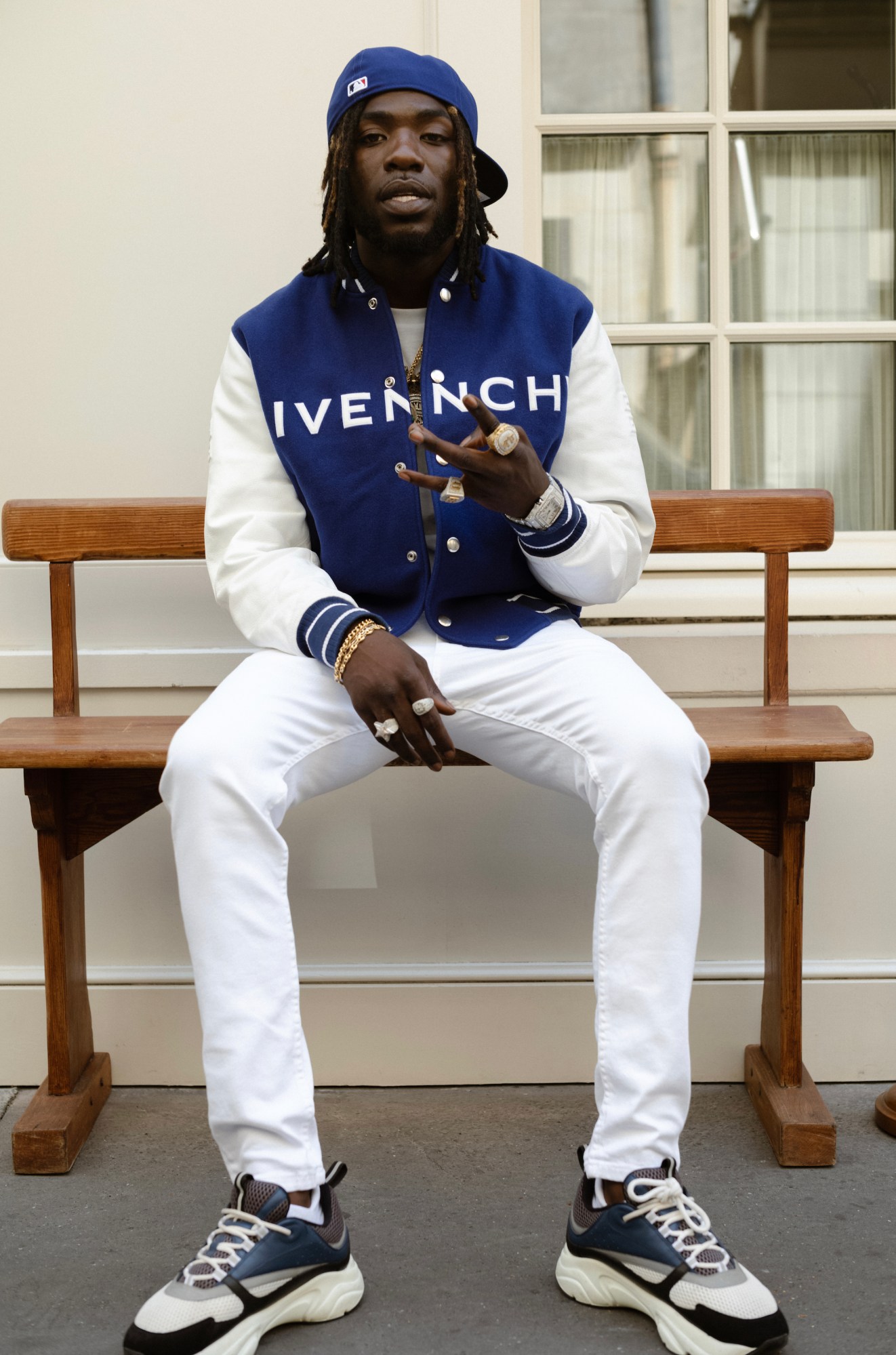 gazo sits on a bench wearing a blue givenchy varsity jacket