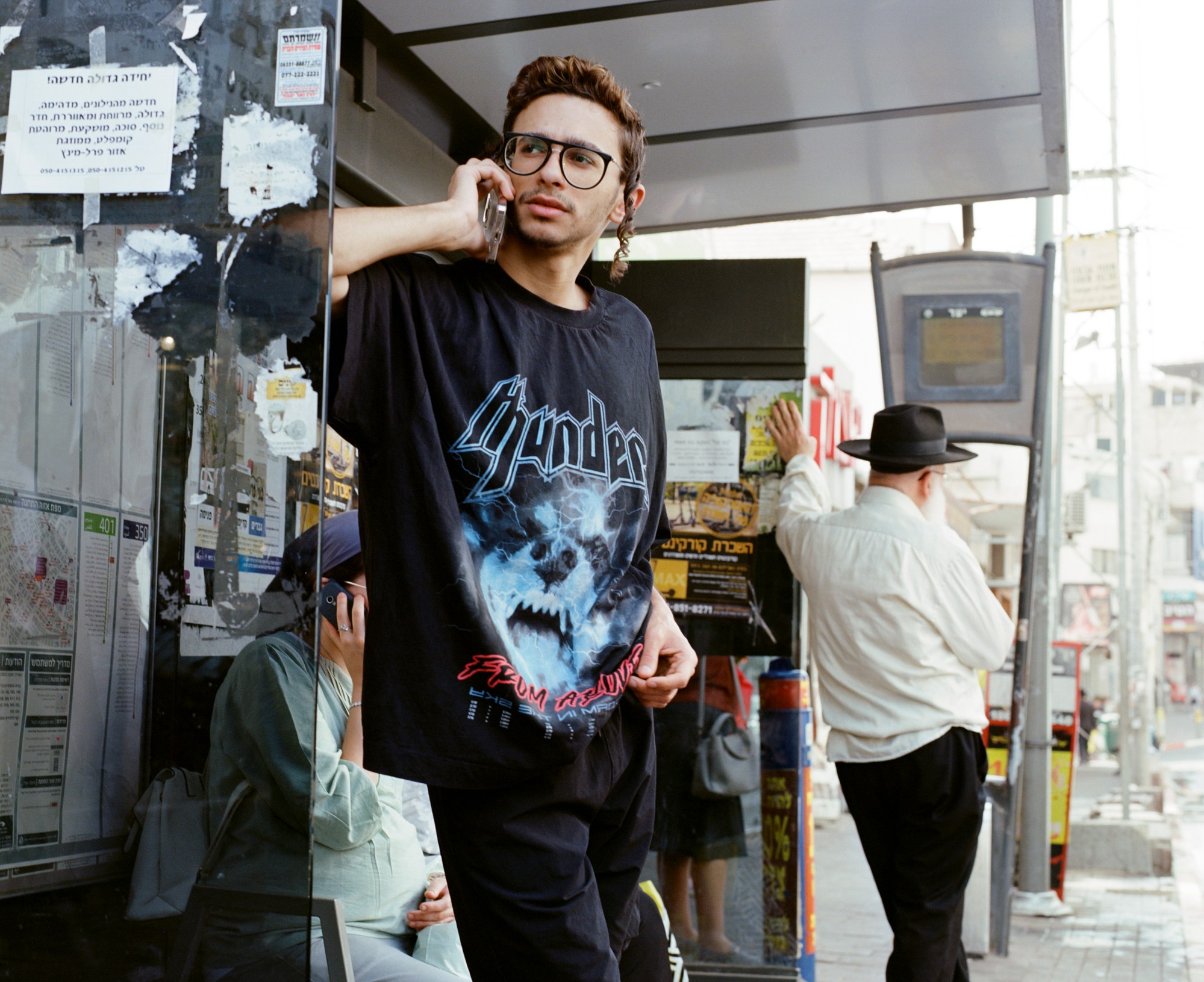 A young Orthodox Jewish man talks on the phone at a bus stop.