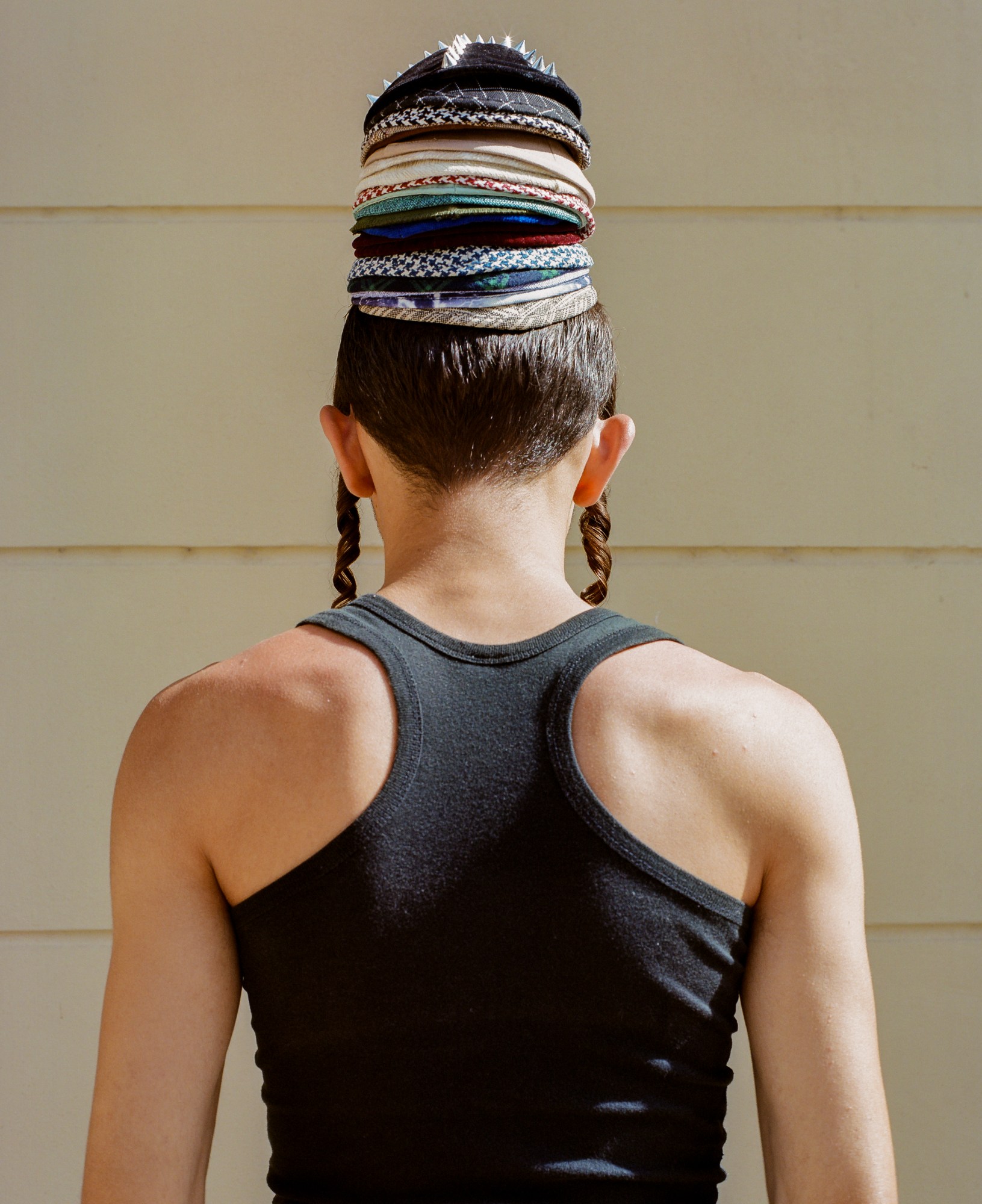 A young Orthodox Jewish man in a black tank top wearing a stack of yarmulkes on his head.