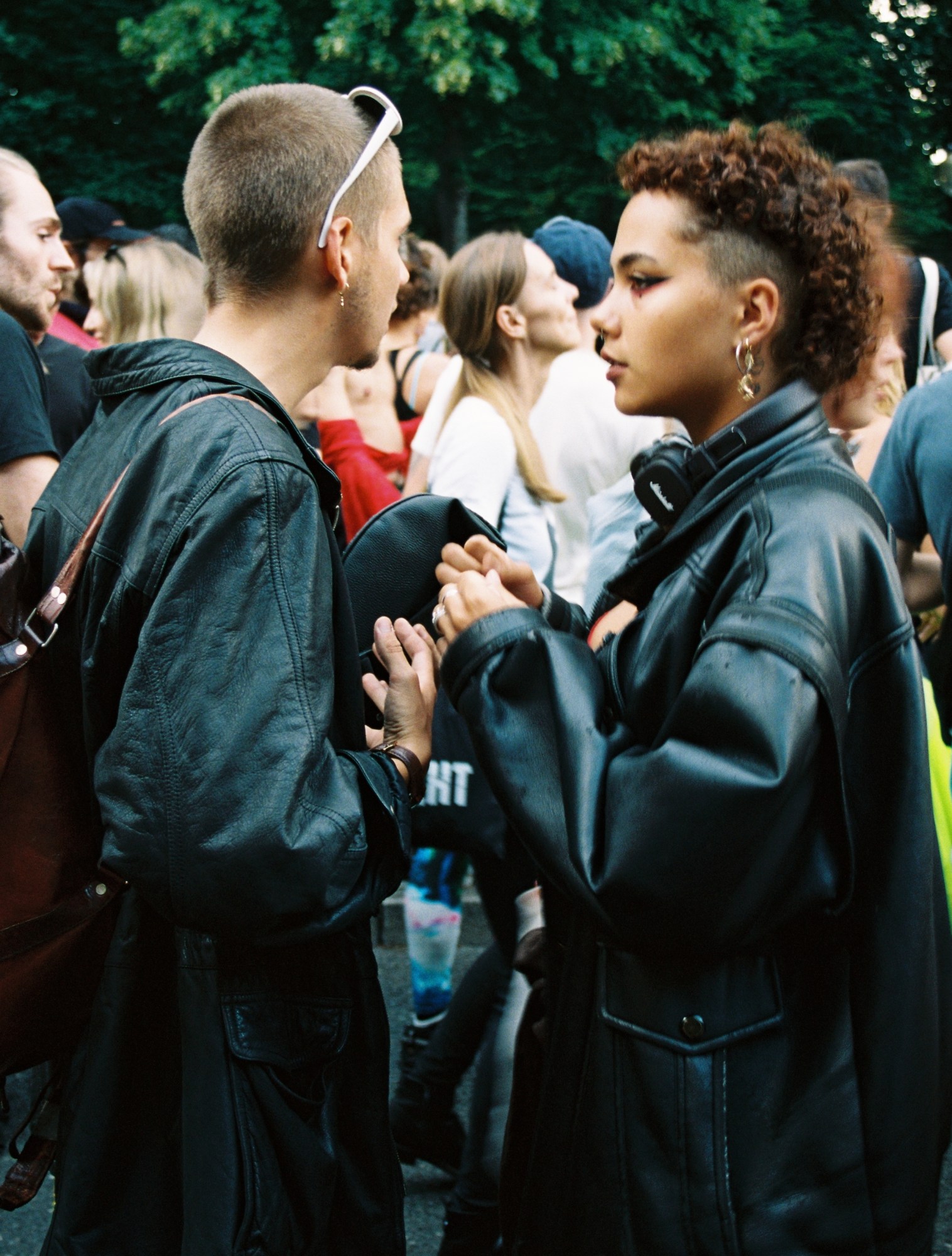 two people wearing oversized leather jackets stand together talking