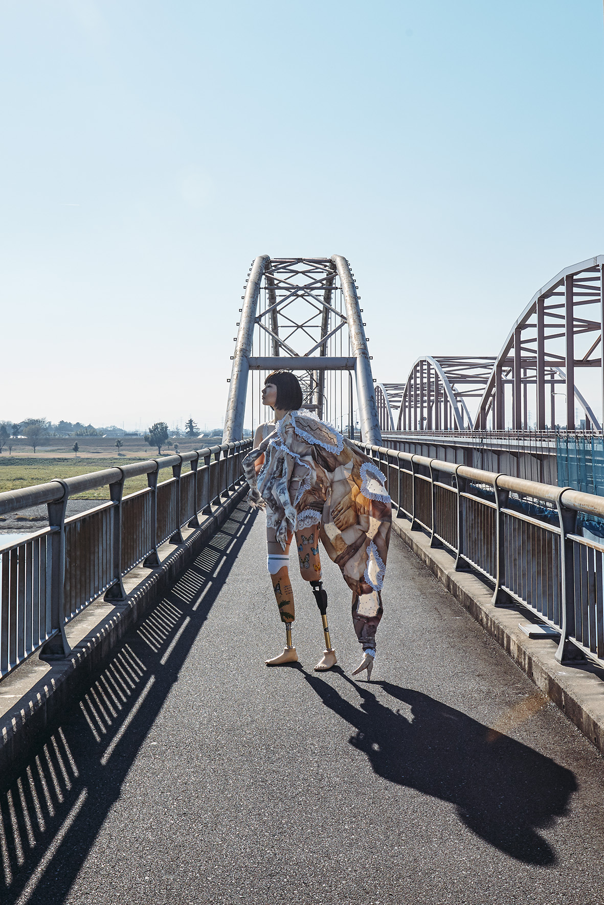 the artist crosses a bridge wearing a costume that gives her an extra-long third leg