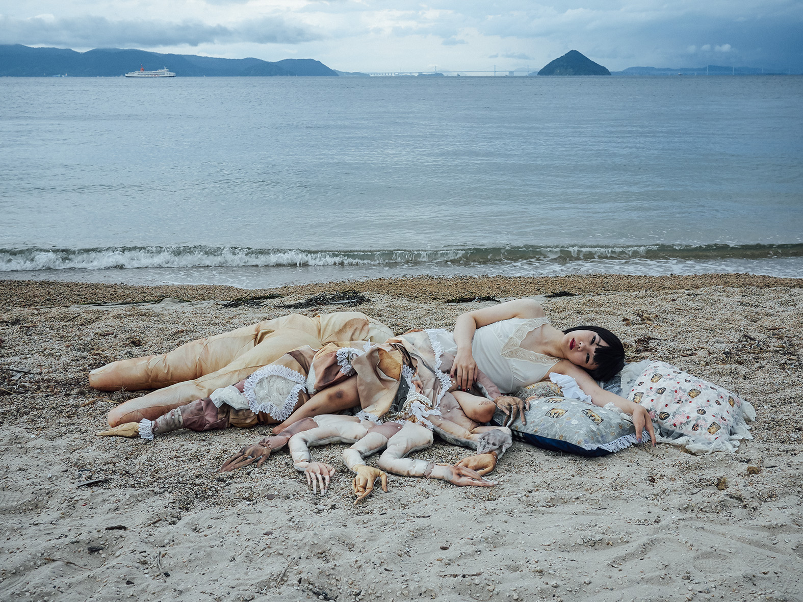 the artist laying on a pile of prosthetic limbs on an empty beach