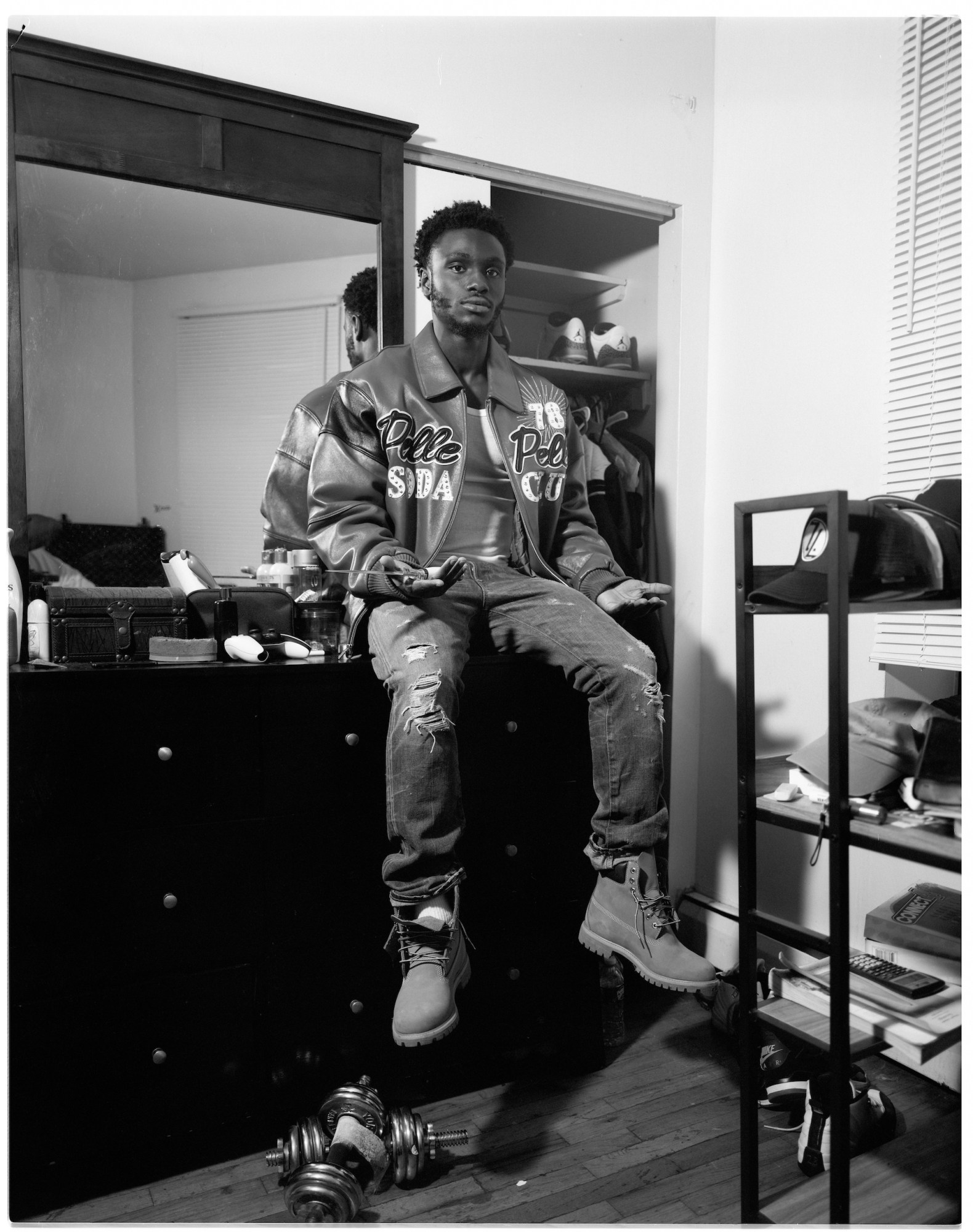 A man wearing Timberland boots and a Pelle Pelle jacket sitting on a dresser holding a knife.