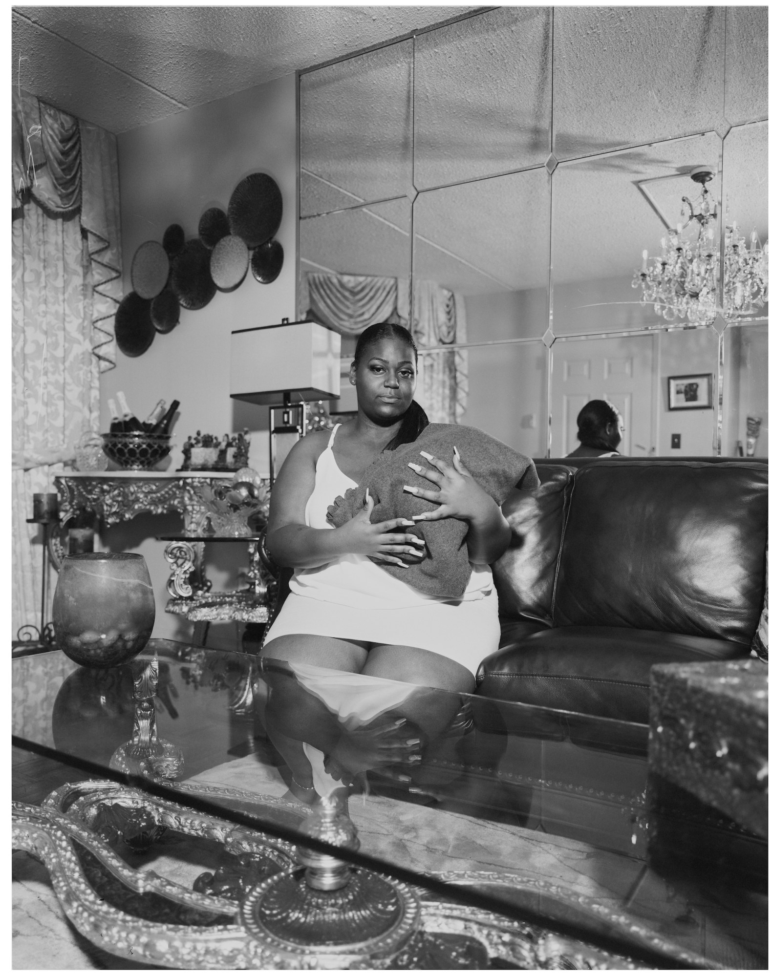 A woman holding a swaddled baby in a living room sitting behing a glass table.