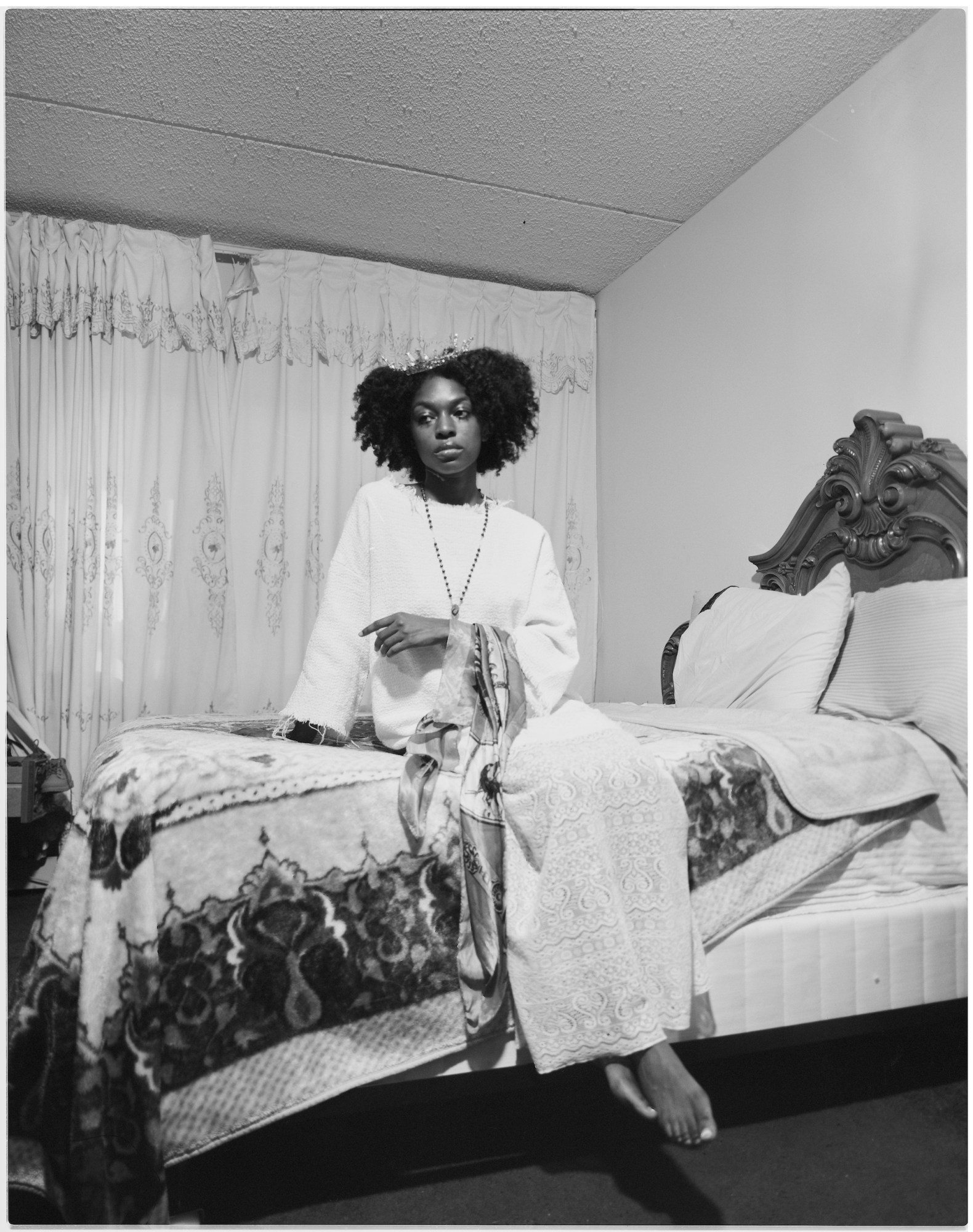 A woman in a white dress sitting on a bed wearing a crown.