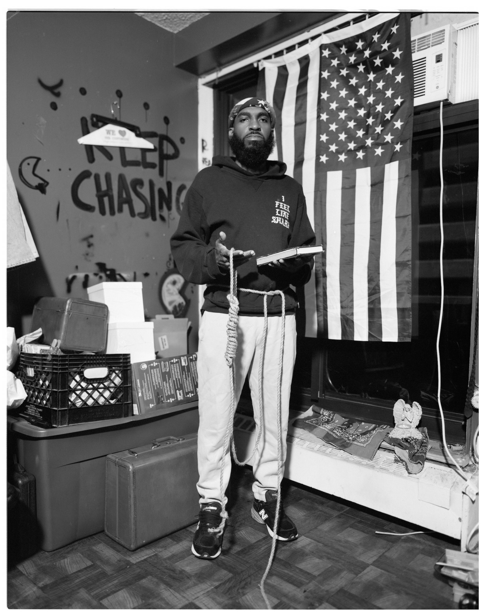 A man wearing sweats and sneakers in front of the American flag holding a noose.