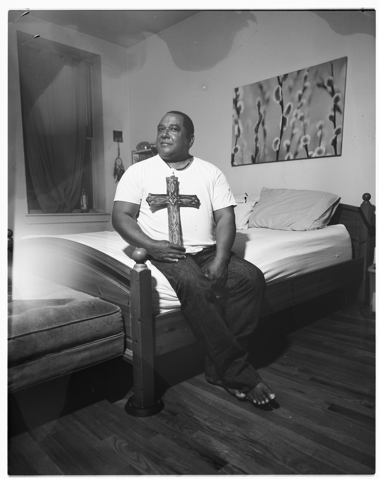 A man sitting on a bed holding a large cross.