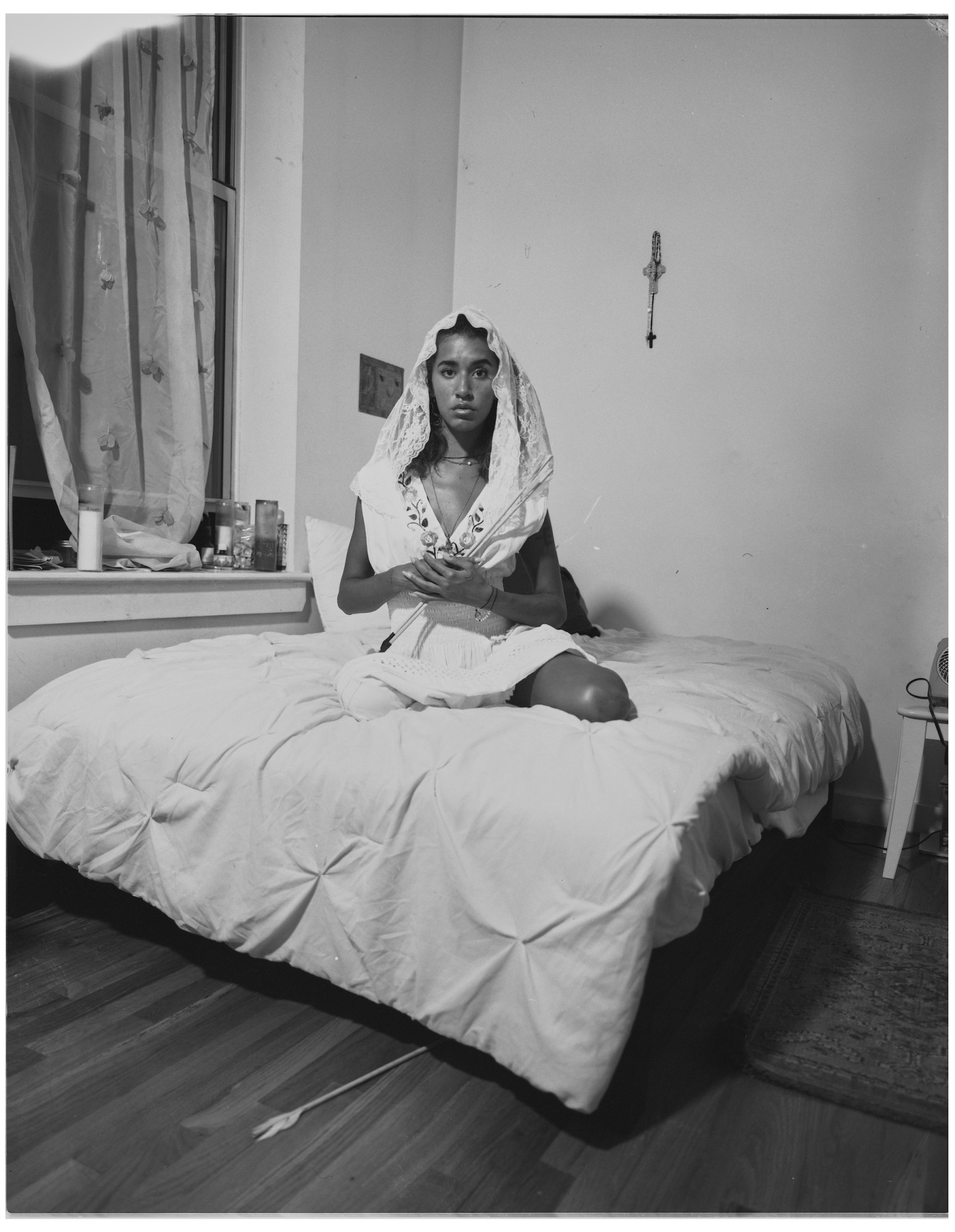 A woman wearing a white scarf and flowers sitting on a bed.