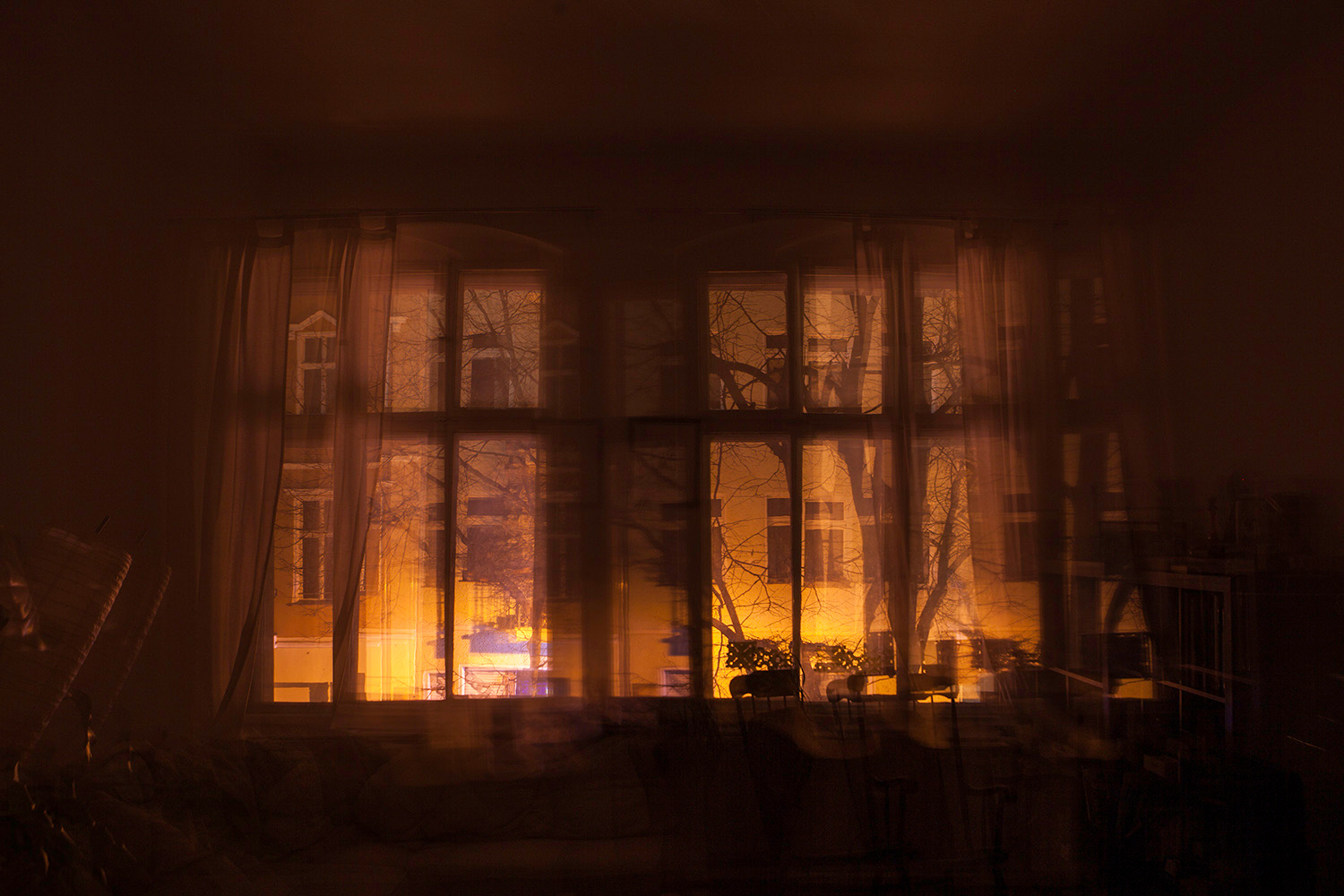 a window covered by curtains in the evening revealing orange glowing light