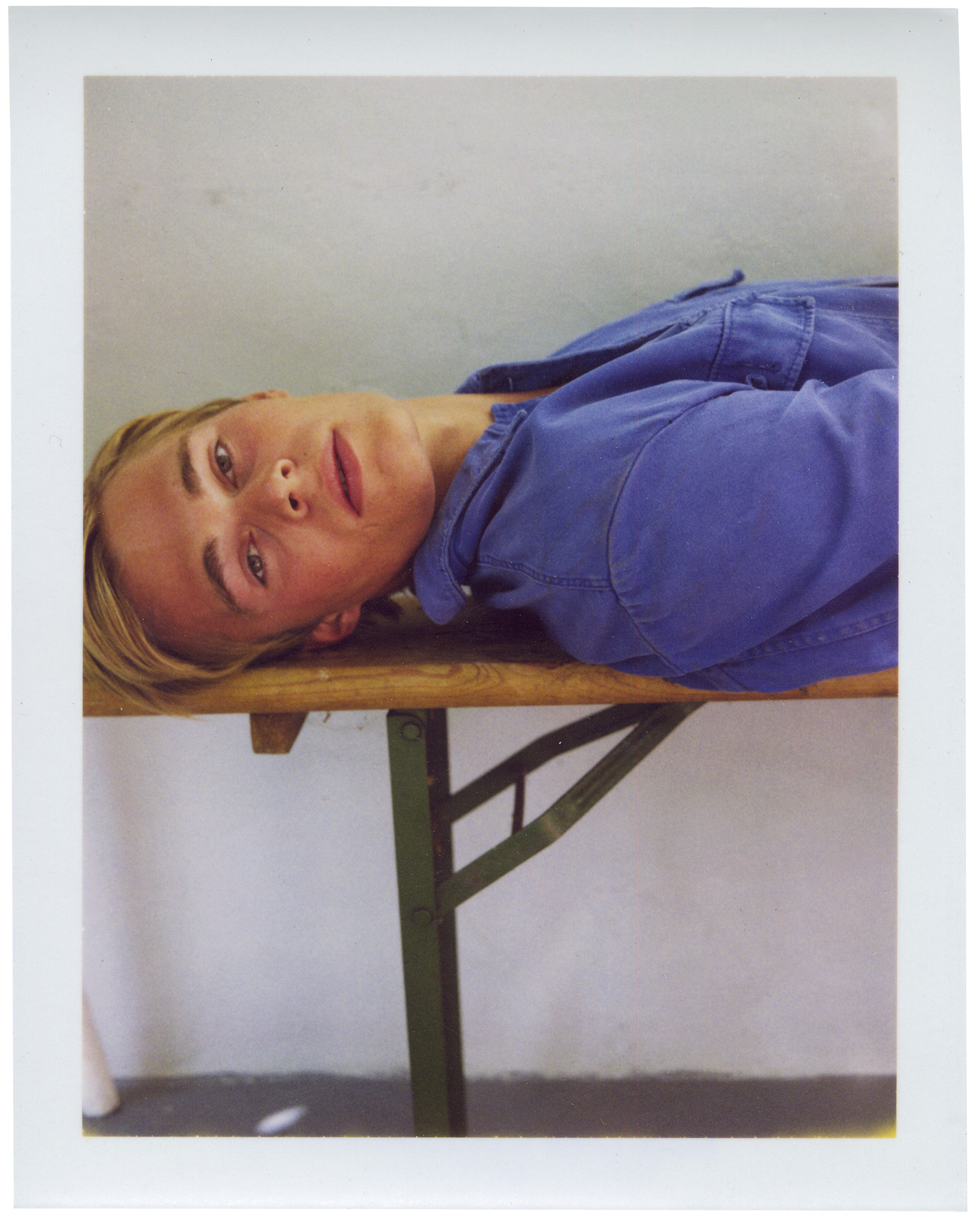 Polaroid of a blonde boy in a blue denim shirt lying on a bench