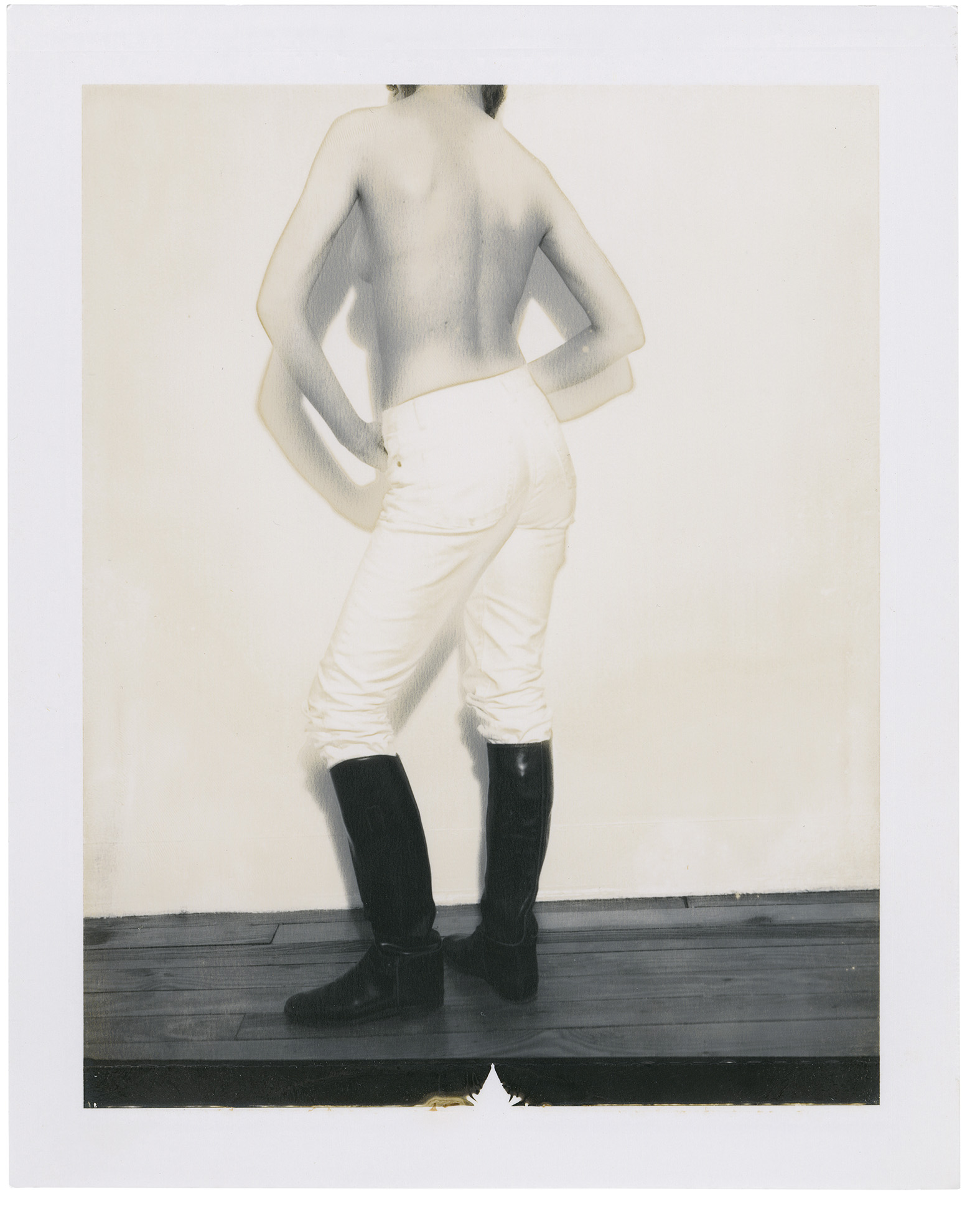 Polaroid of a man below his head from behind wearing white trousers and military boots.