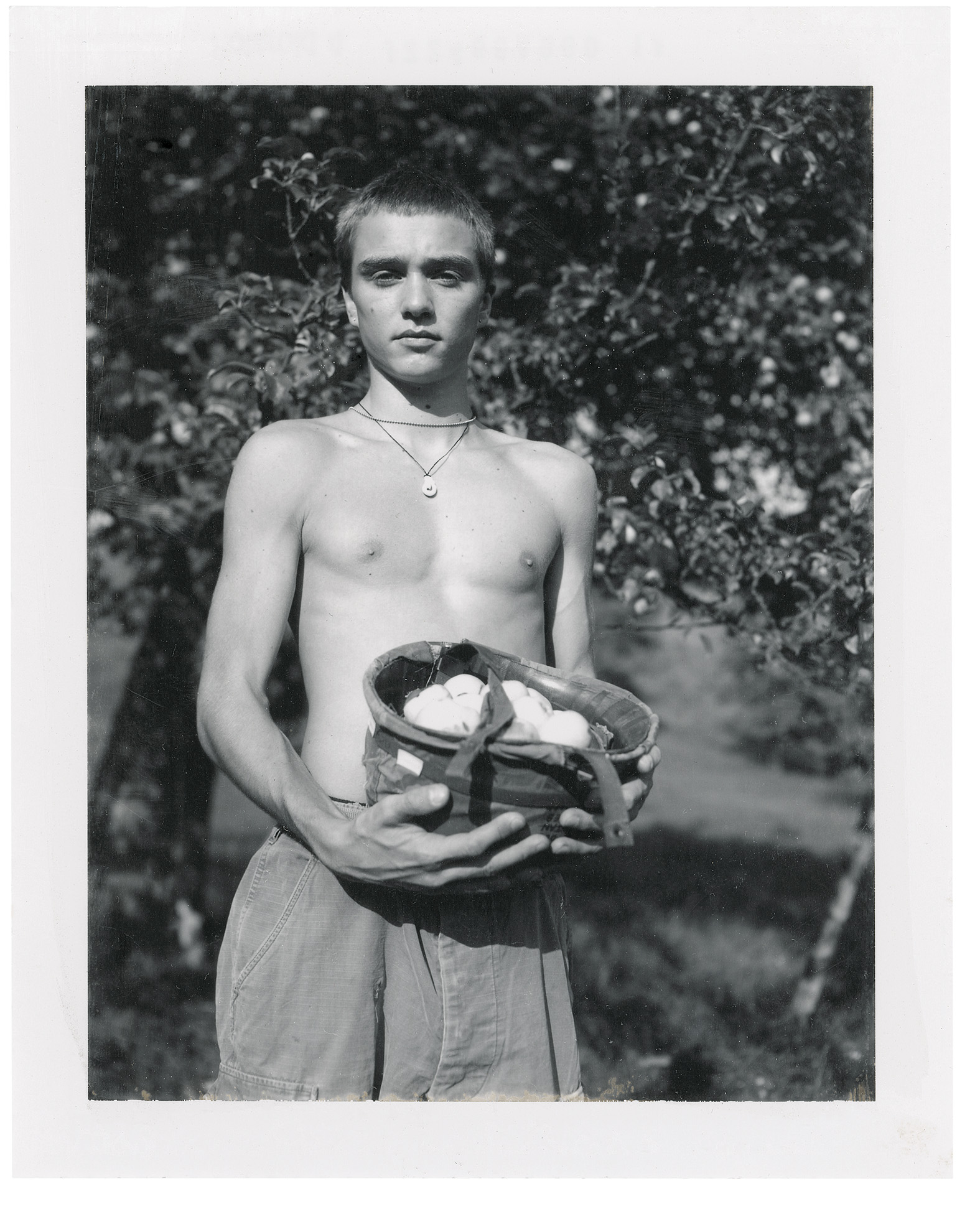 Photo of a shirtless boy outside collecting plants in an old German military helmet.