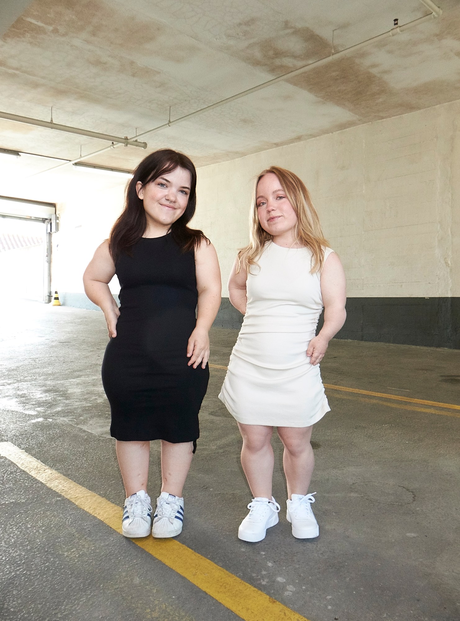 Two little people stood on a concrete floor, wearing bodycon dresses in black and white