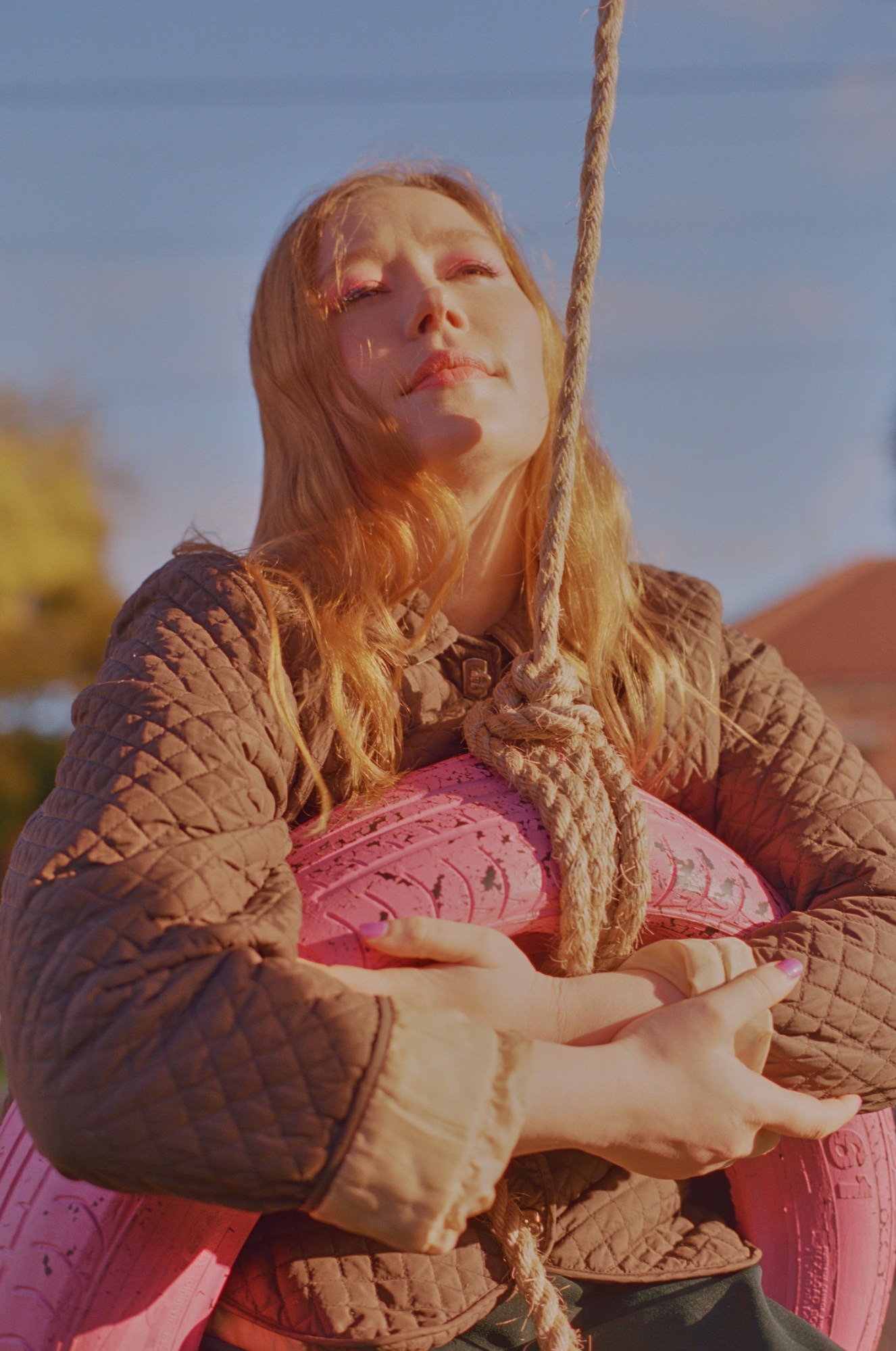 julia jacklin swinging on a pink tire swing under the blue sky