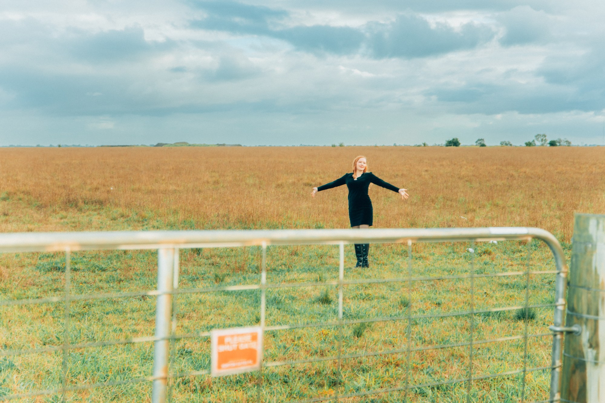 julia jacklin in an open green field with her arms spread out to the side