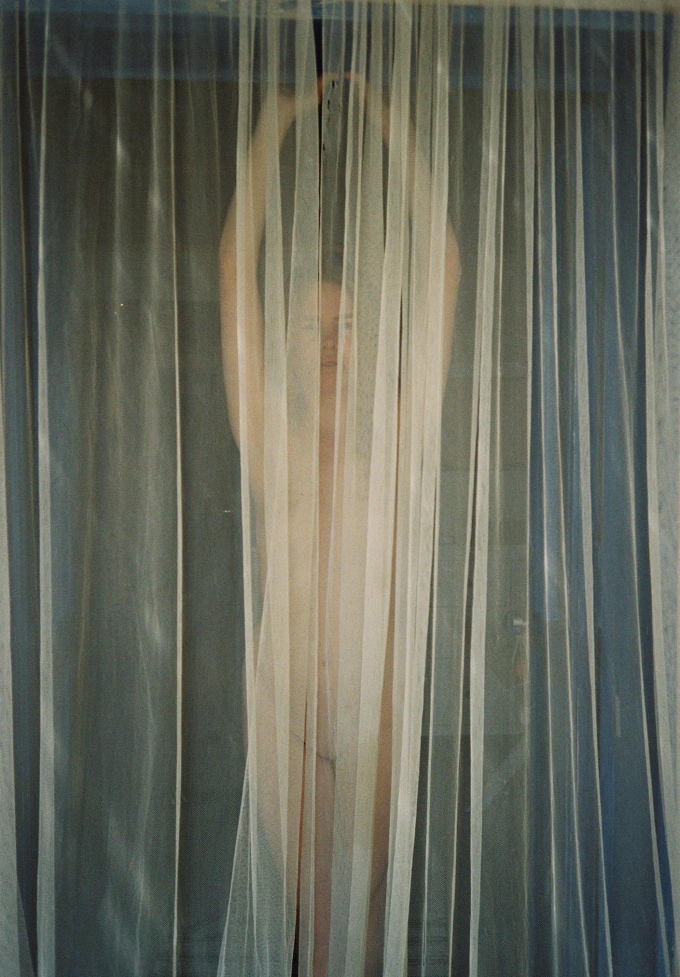 a woman's nude body is half visible through a light net curtain