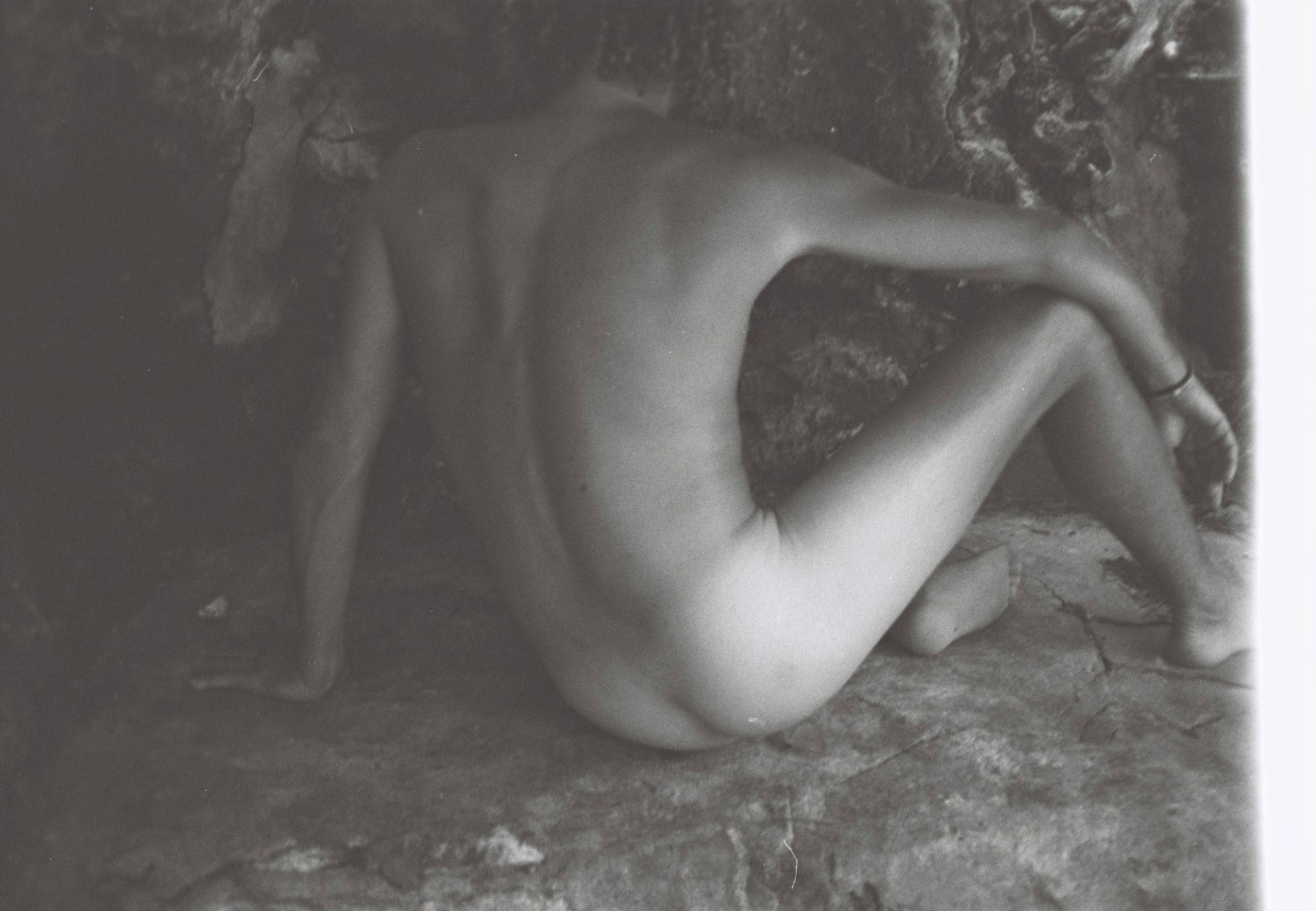 a nude body sitting down in a cave, taken from behind, in black and white