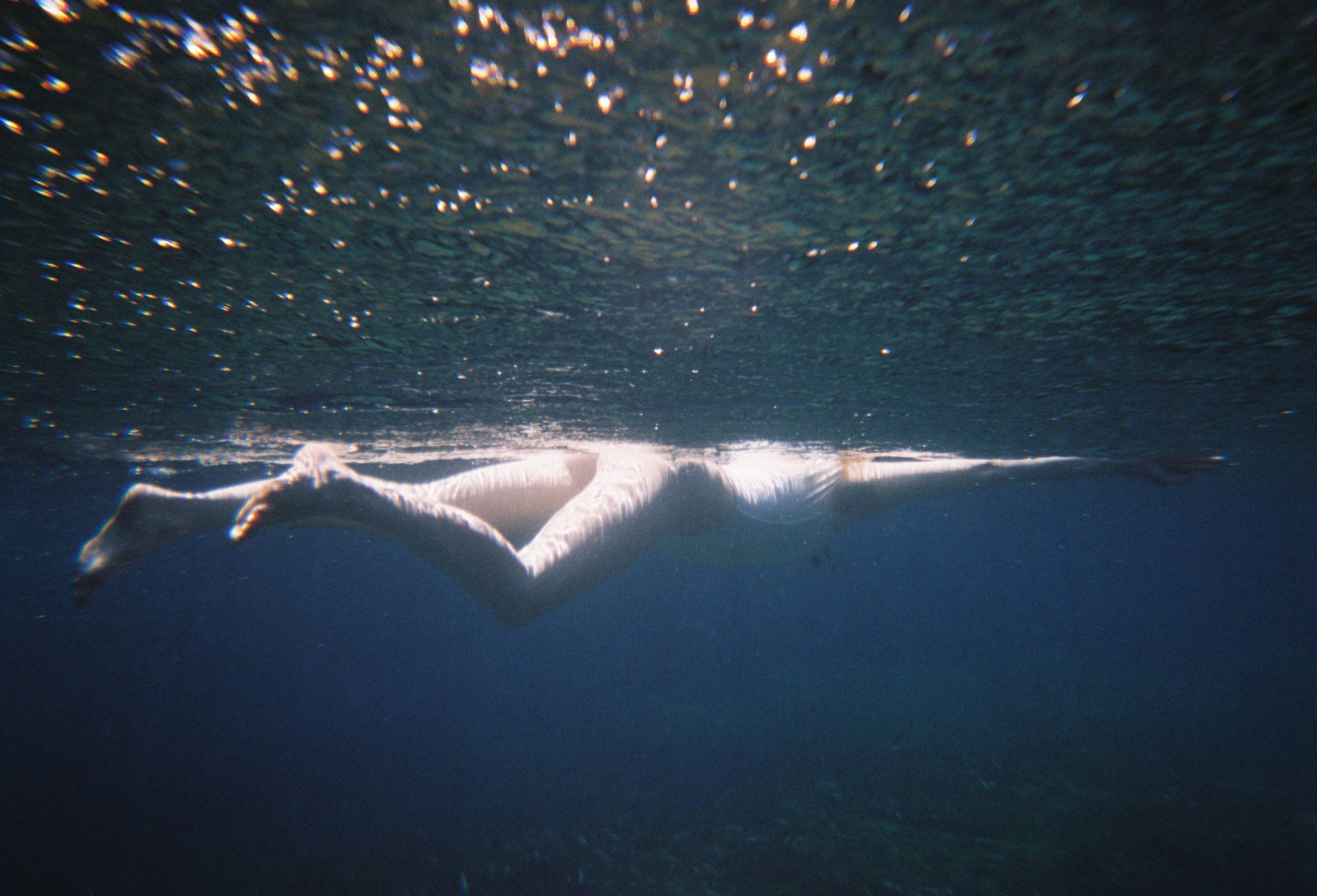 an underwater photograph of a body floating just beneath the surface of the sea, the sunlight streaming down