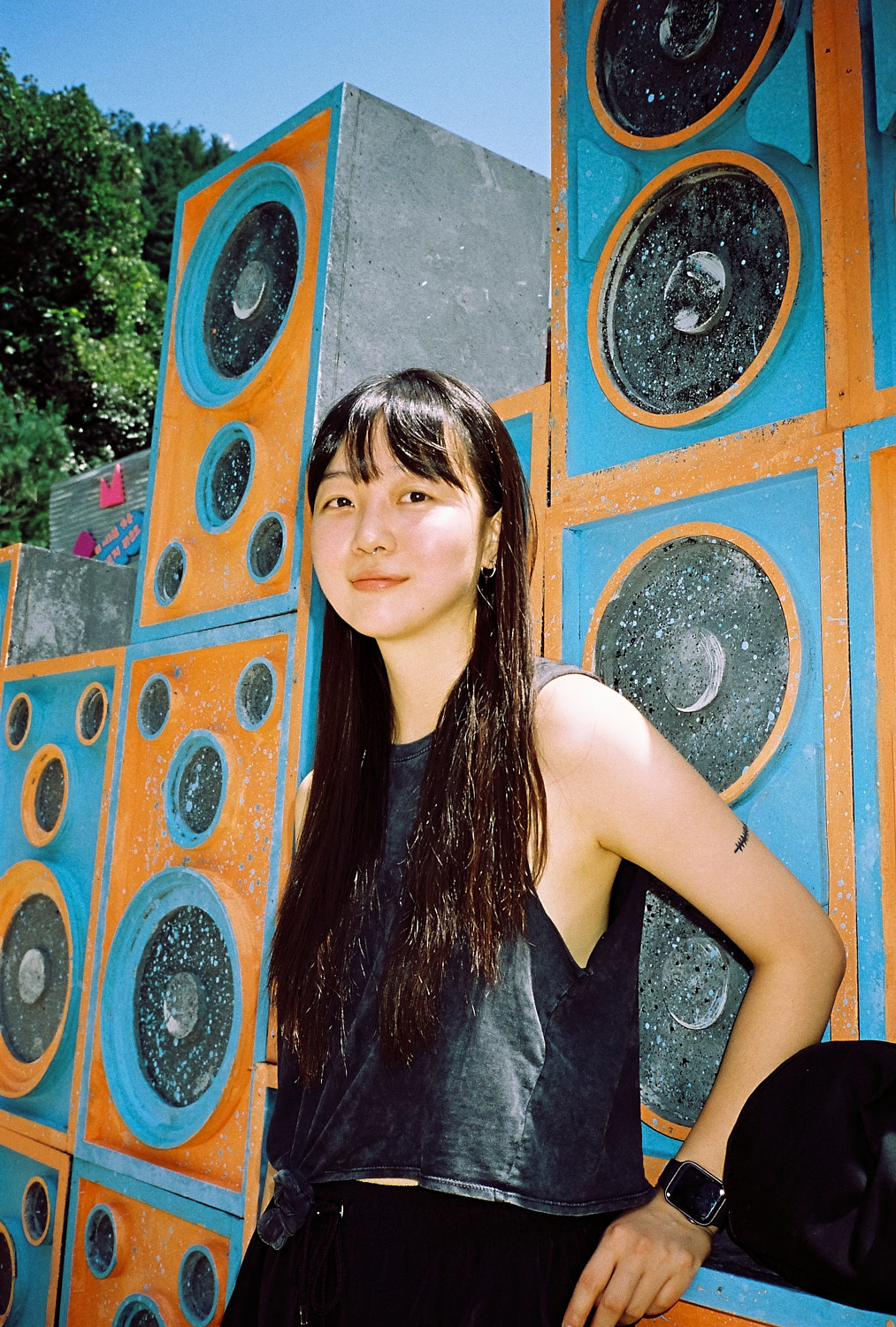 a woman with long dark hair poses in front of a colourful speaker wall