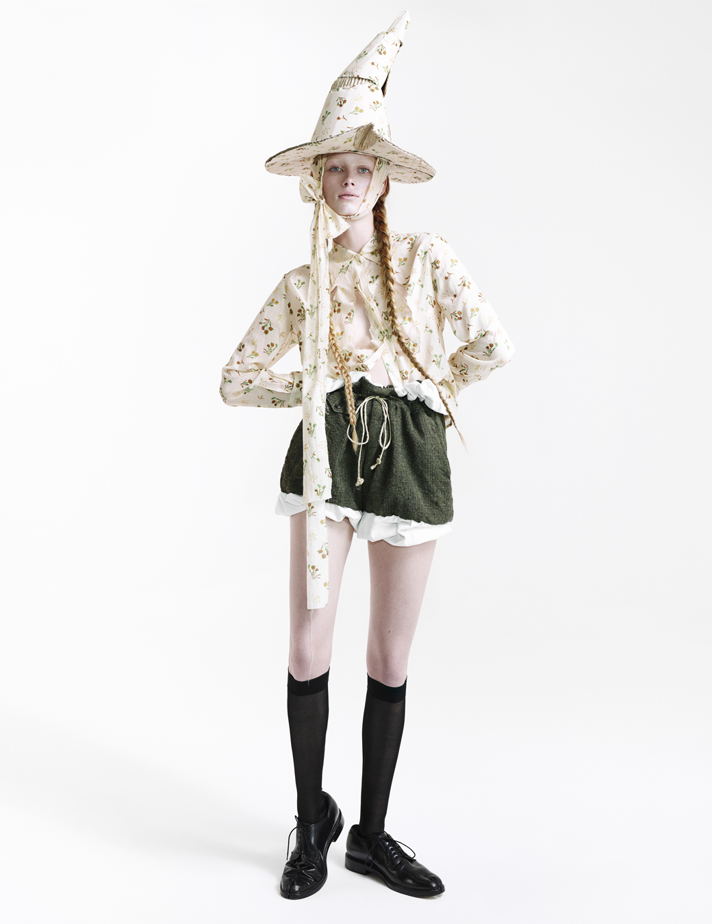 Rianne Van Rompaey dressed in a witch's hat, green shorts, floral blouse, black socks and black shoes in I-D The Ultra! Issue Fall 2022, photographed by Willy Vanderperre and styled by Olivier Rizzo