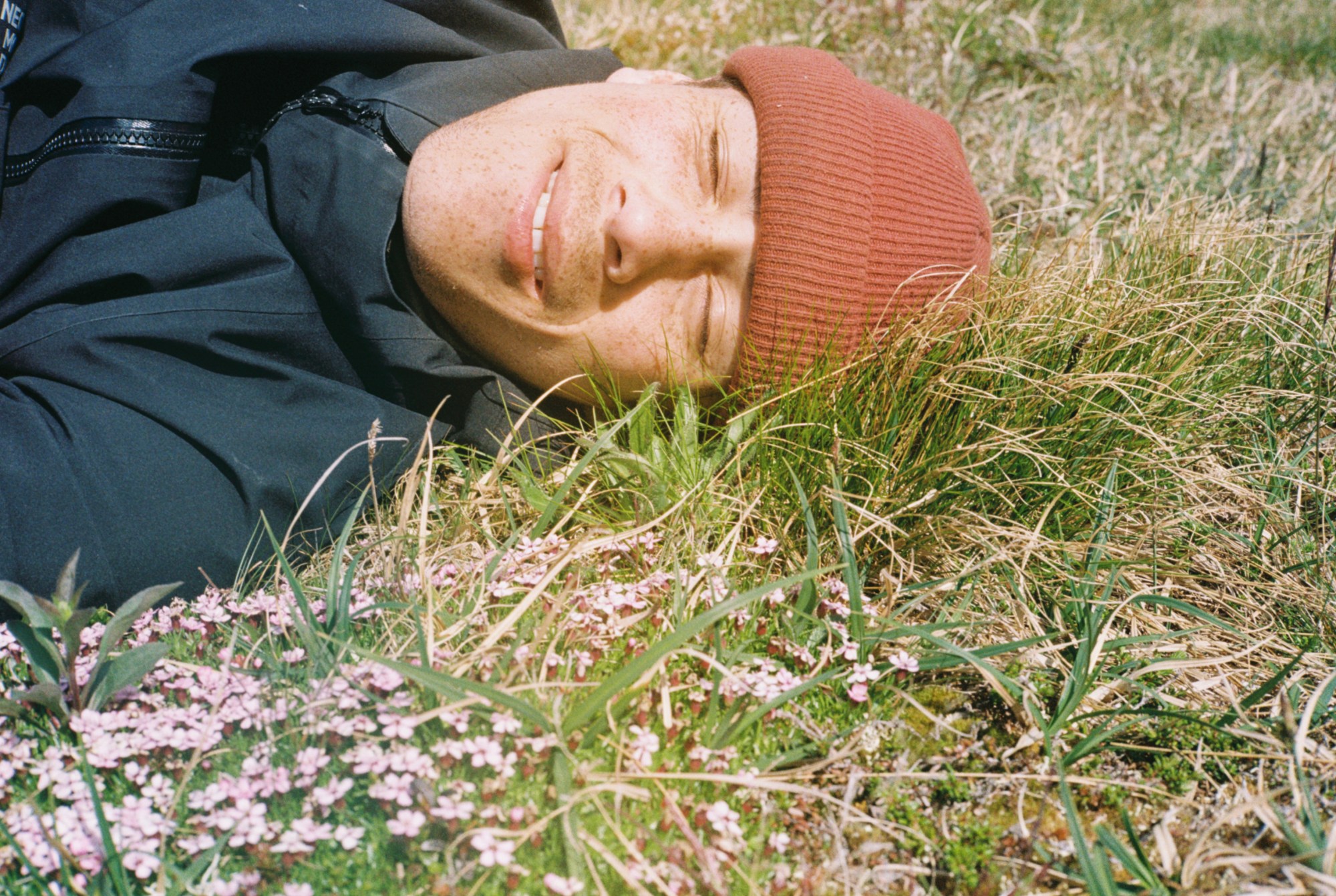 a man wearing an orange beanie lies on the grass