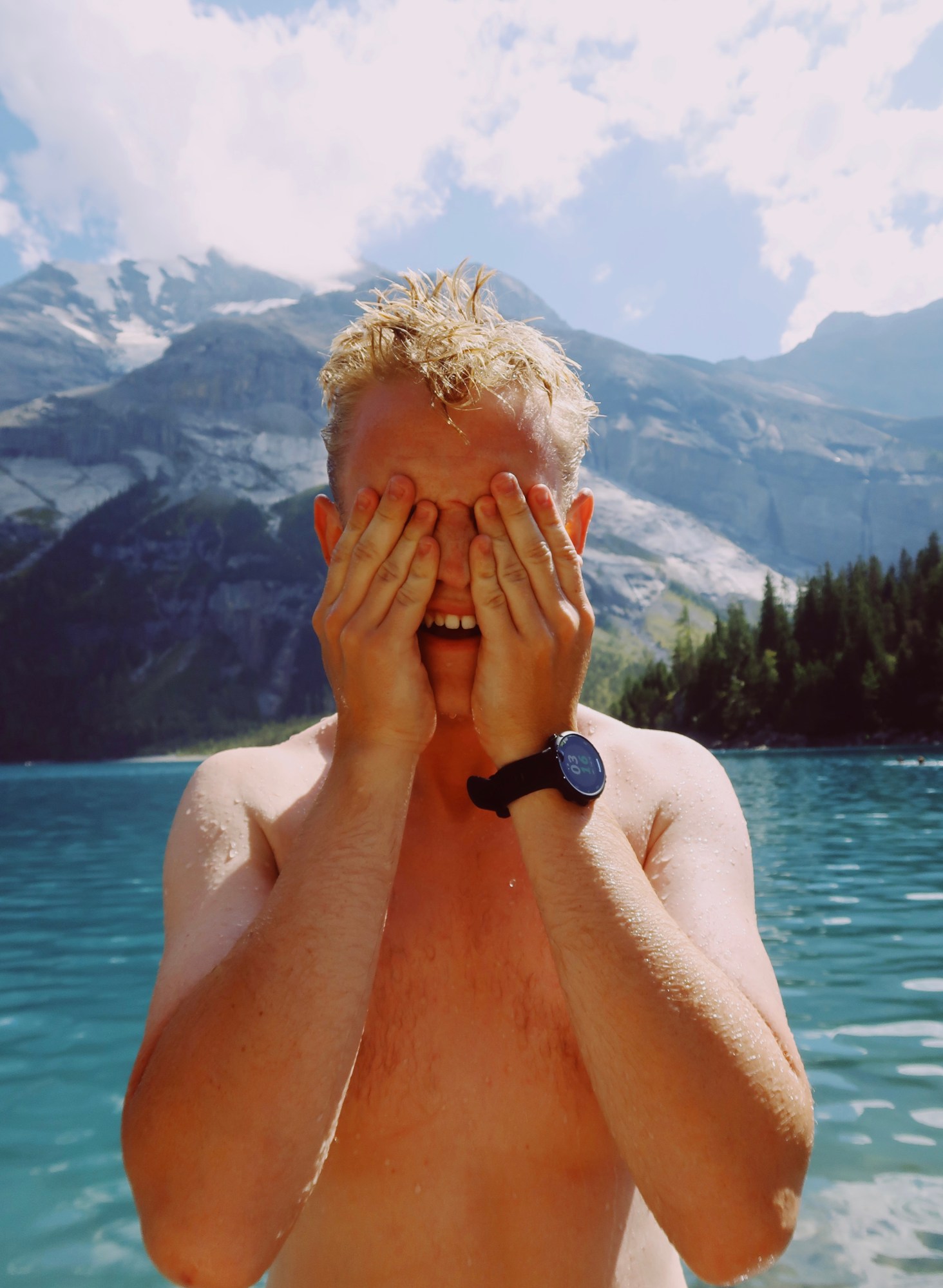 a topless man in a blue water covers his eyes with his hands