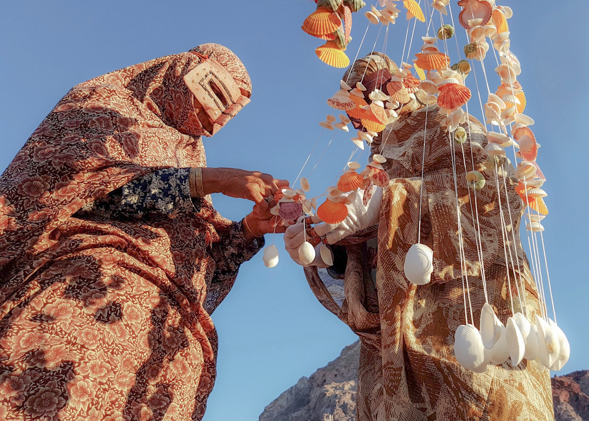 two woman in costume make jewellery out of shells