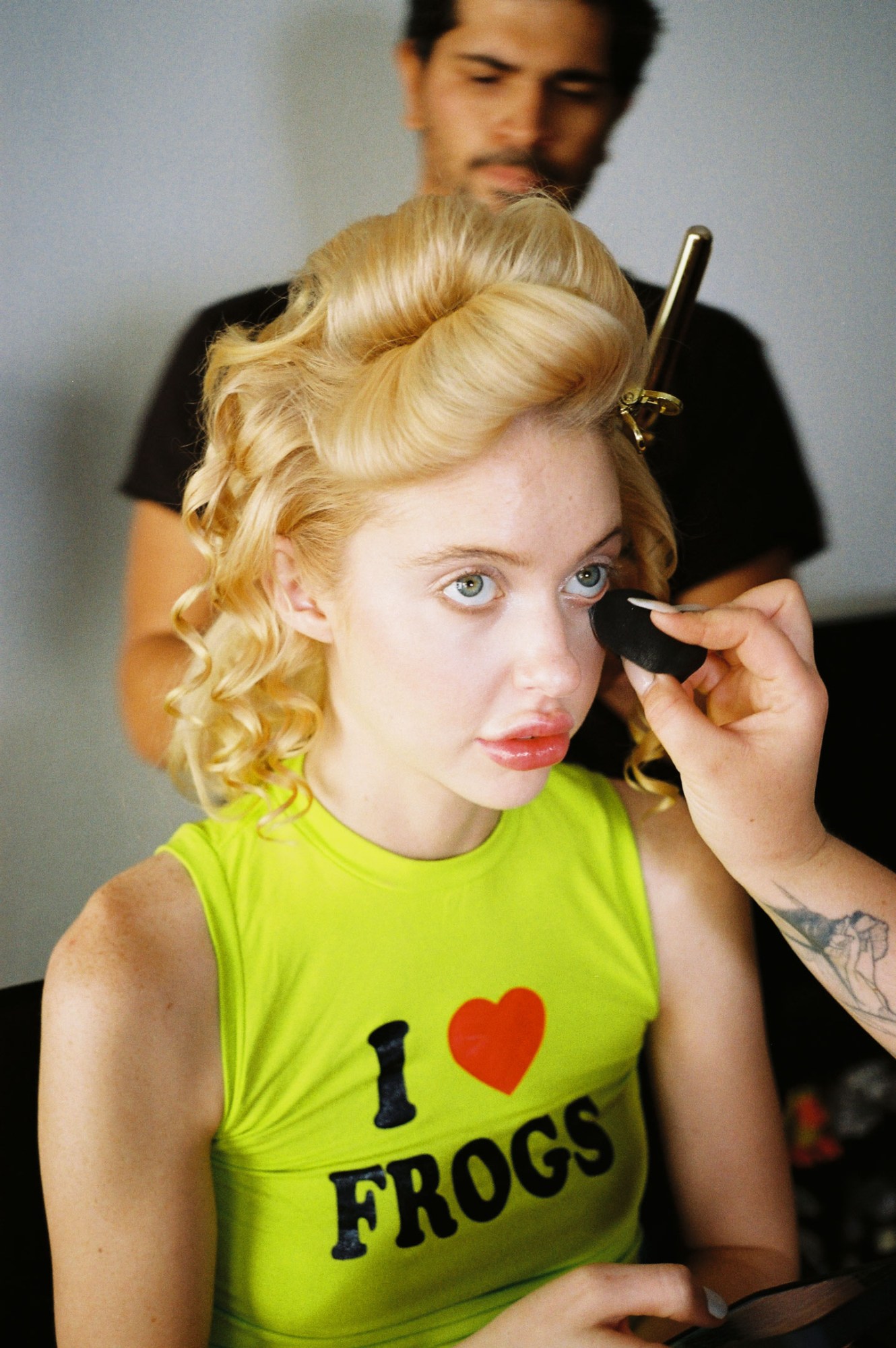 a close up of chloe cherry in a fluorescent yellow tank top, having her makeup done