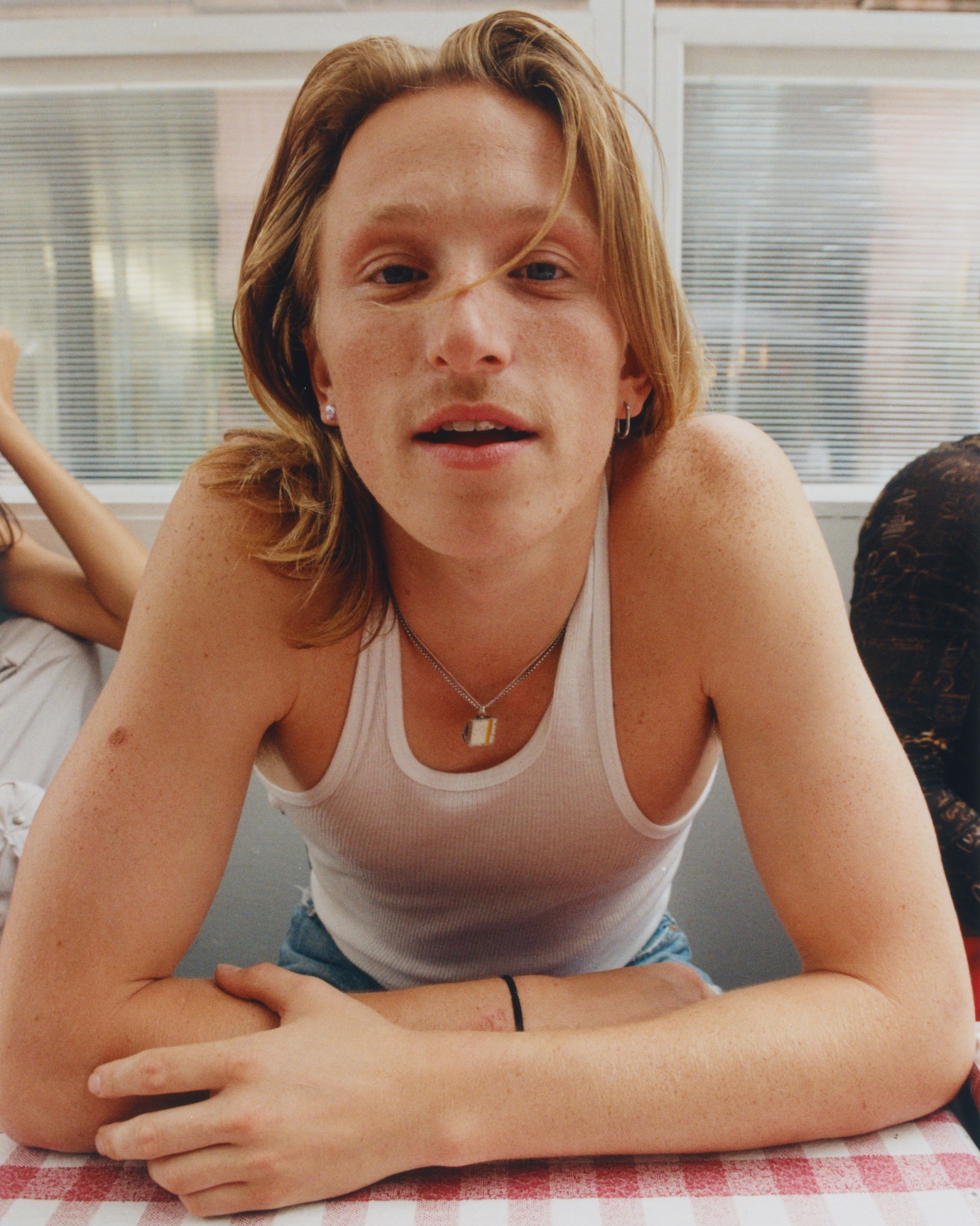 ben hard wearing a white tank top and sitting with arms crossed at a checkered table