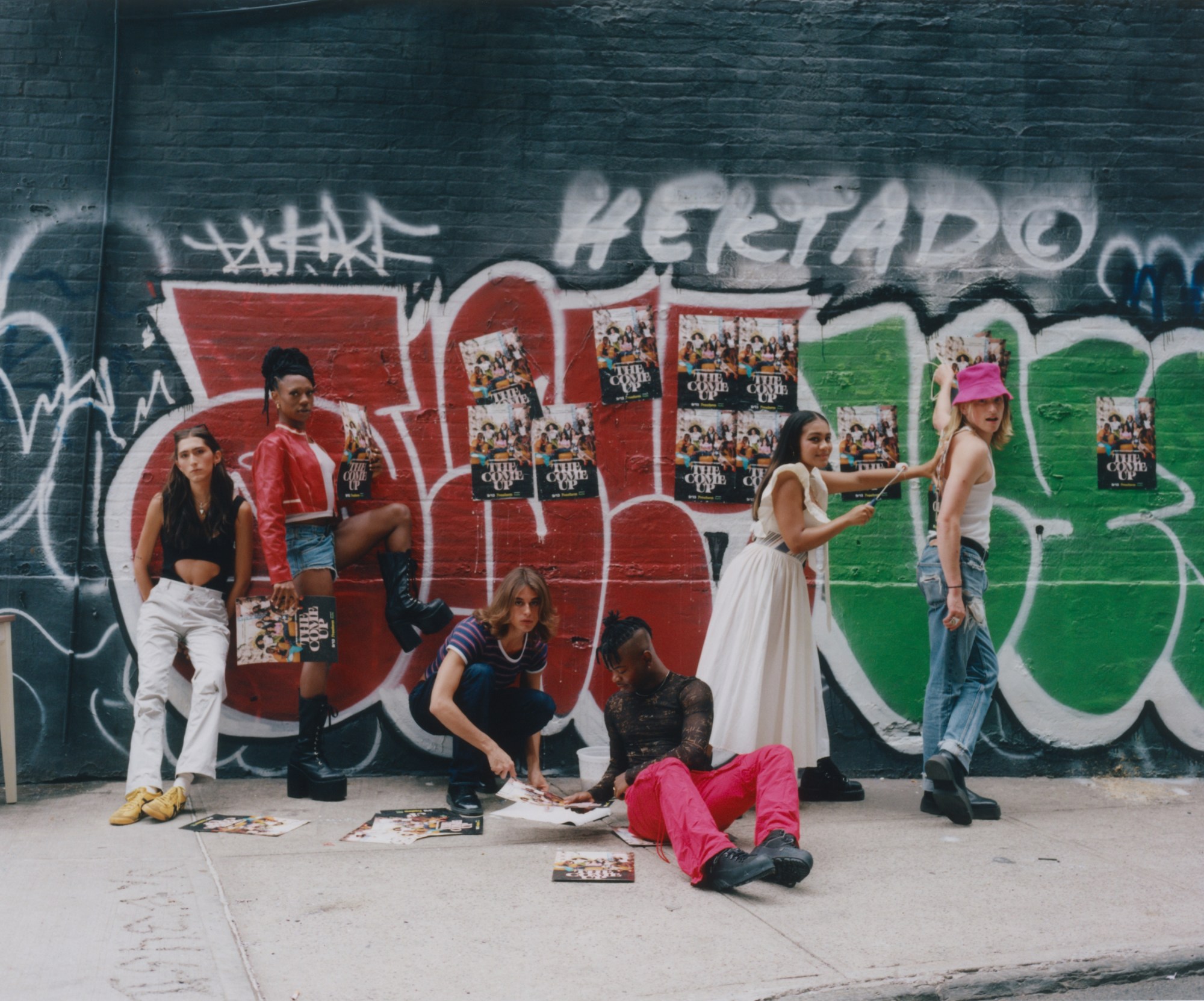 the cast of freeform's the come up wheatpasting posters on a graffiti covered wall in new york